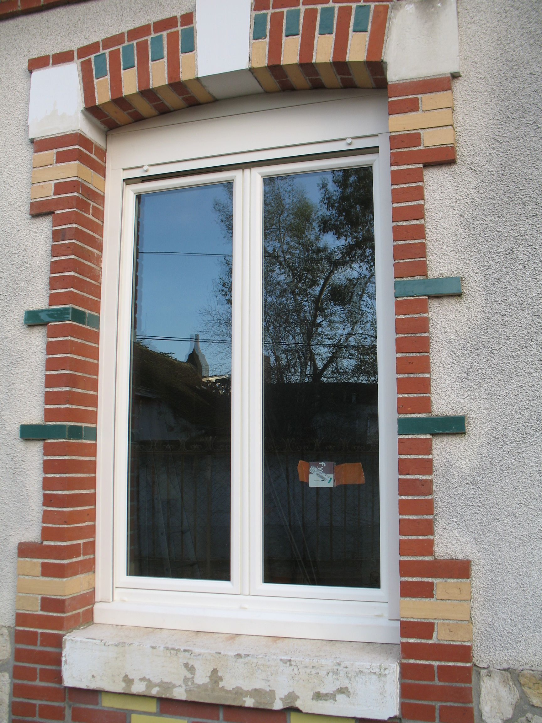 Fenêtre avec cadre blanc, arbres reflétés et encadrement en brique et pierre.