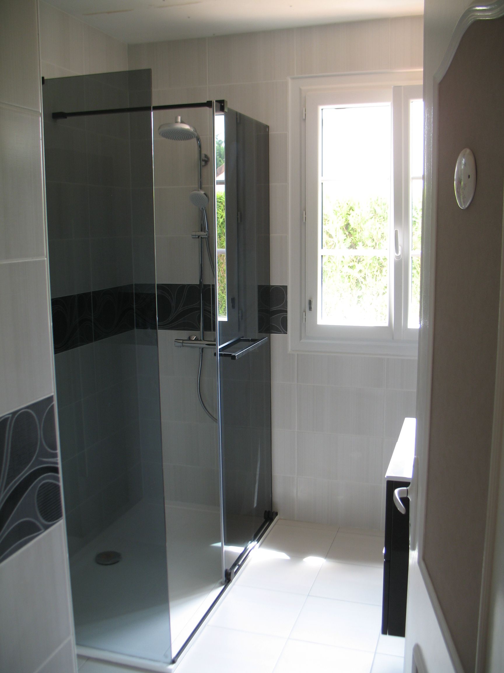 Salle de bain avec cabine de douche grise, carrelage blanc et fenêtre.