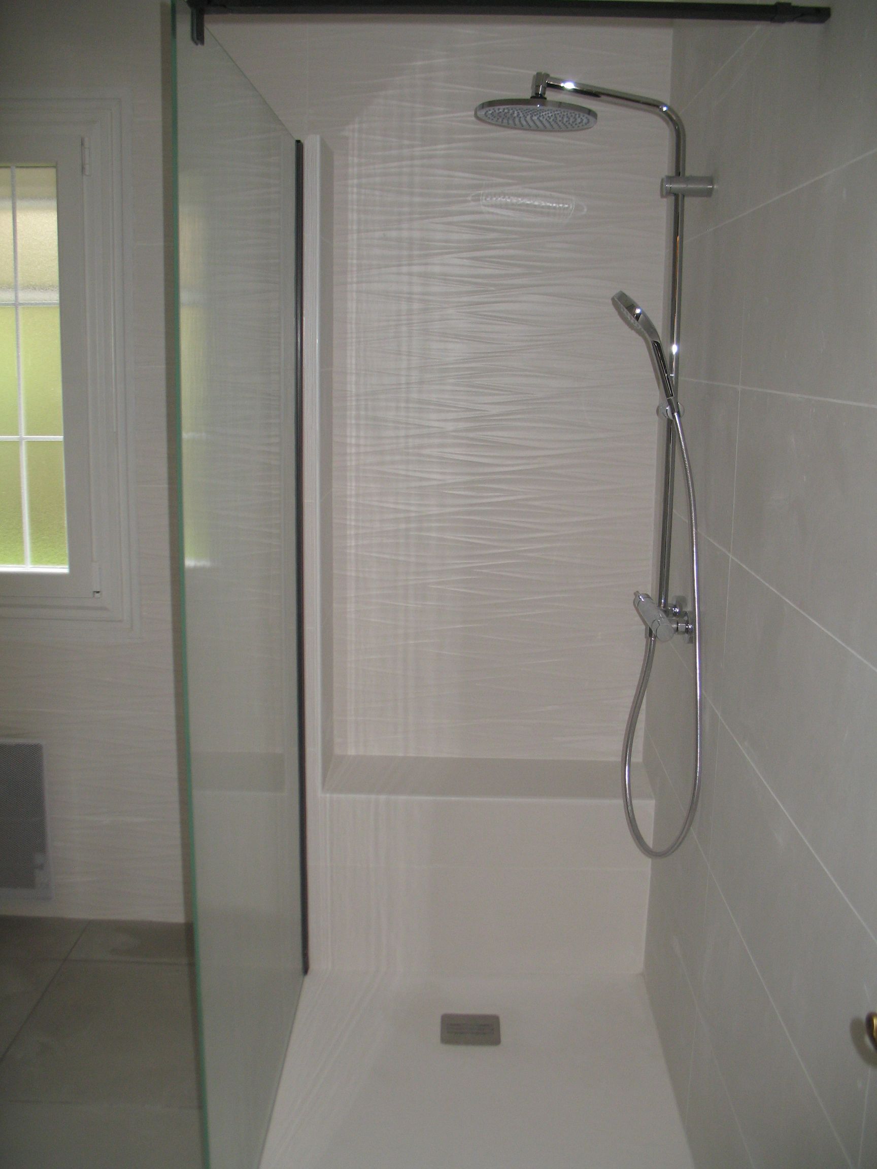 Douche avec porte vitrée, murs blancs, luminaires chromés et fenêtre avec stores.