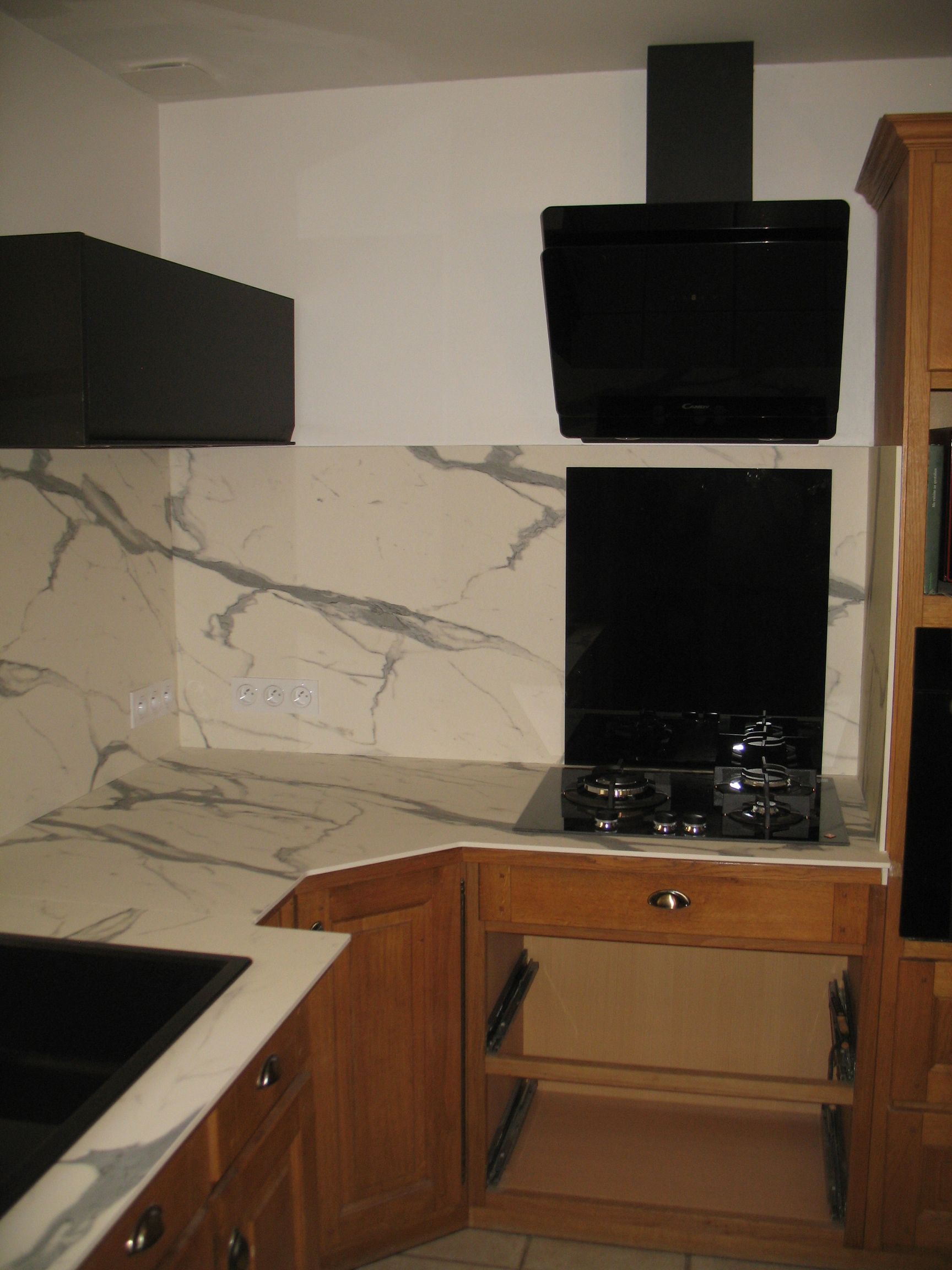 Coin cuisine avec dosseret en marbre, hotte noire et armoires en bois.