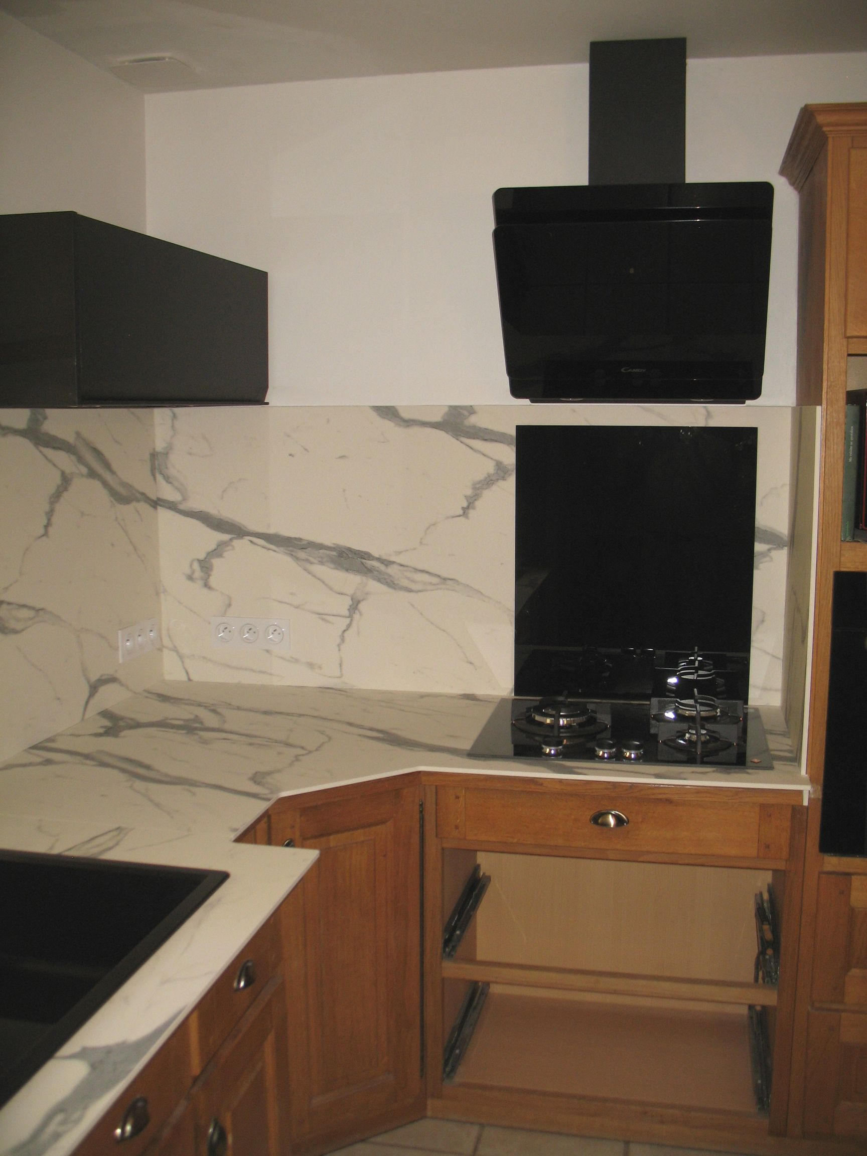 Cuisine avec dosseret en marbre, hotte et four noirs et armoires en bois.