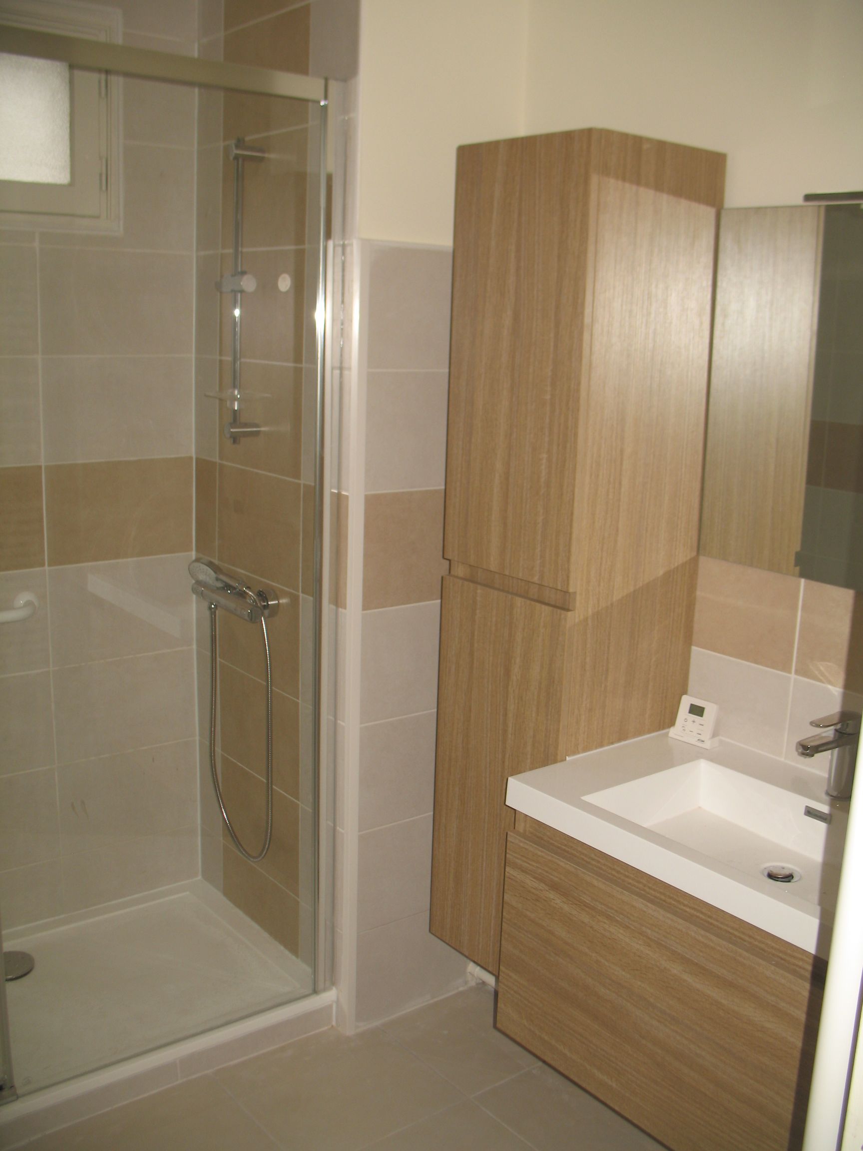 Salle de bain avec douche, lavabo et meuble haut. Carrelage beige et finition bois clair.