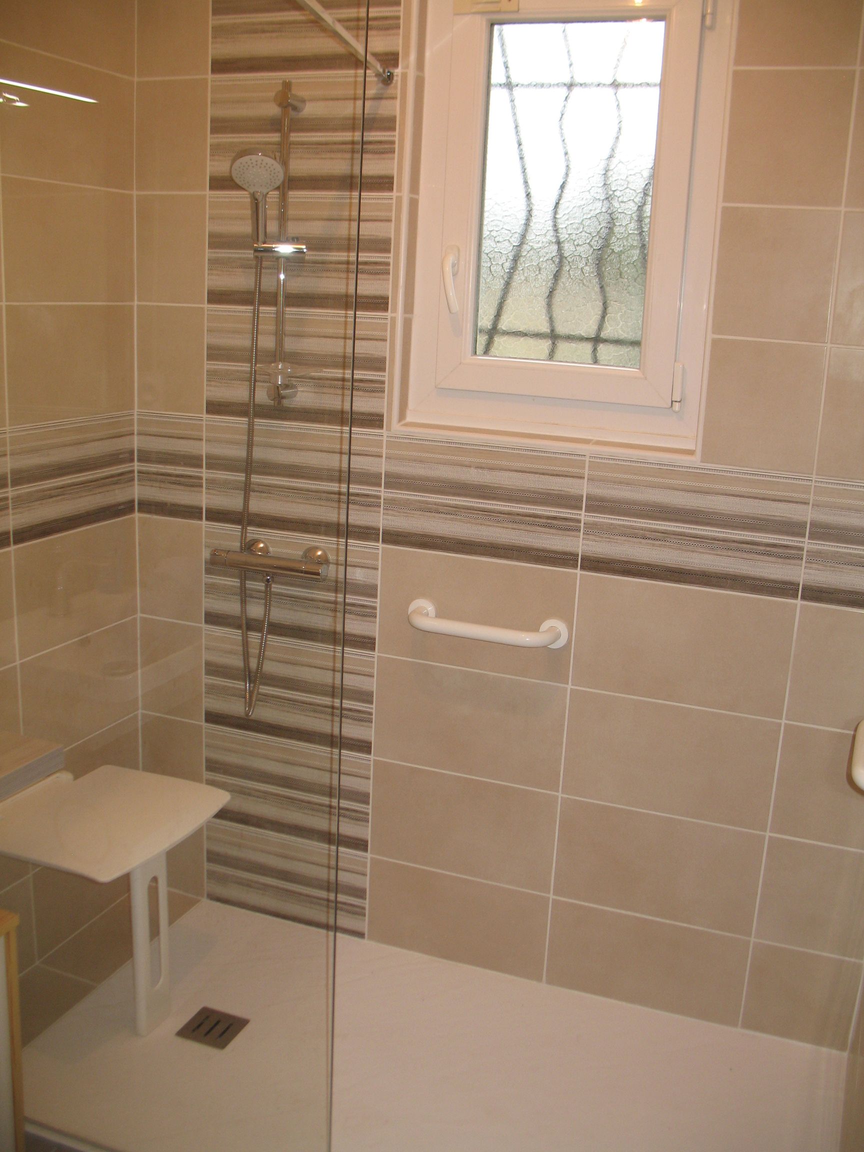Douche accessible avec siège, barre d'appui et bande de carrelage décorative.