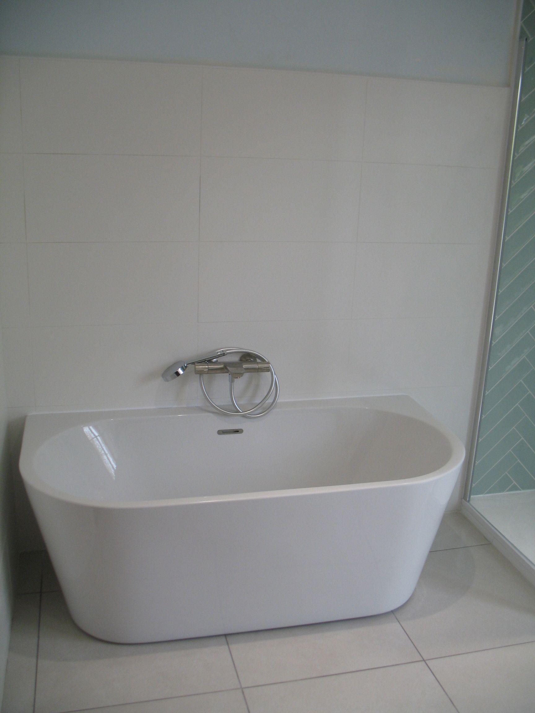 Baignoire autoportante blanche avec robinet chromé contre un mur carrelé blanc.