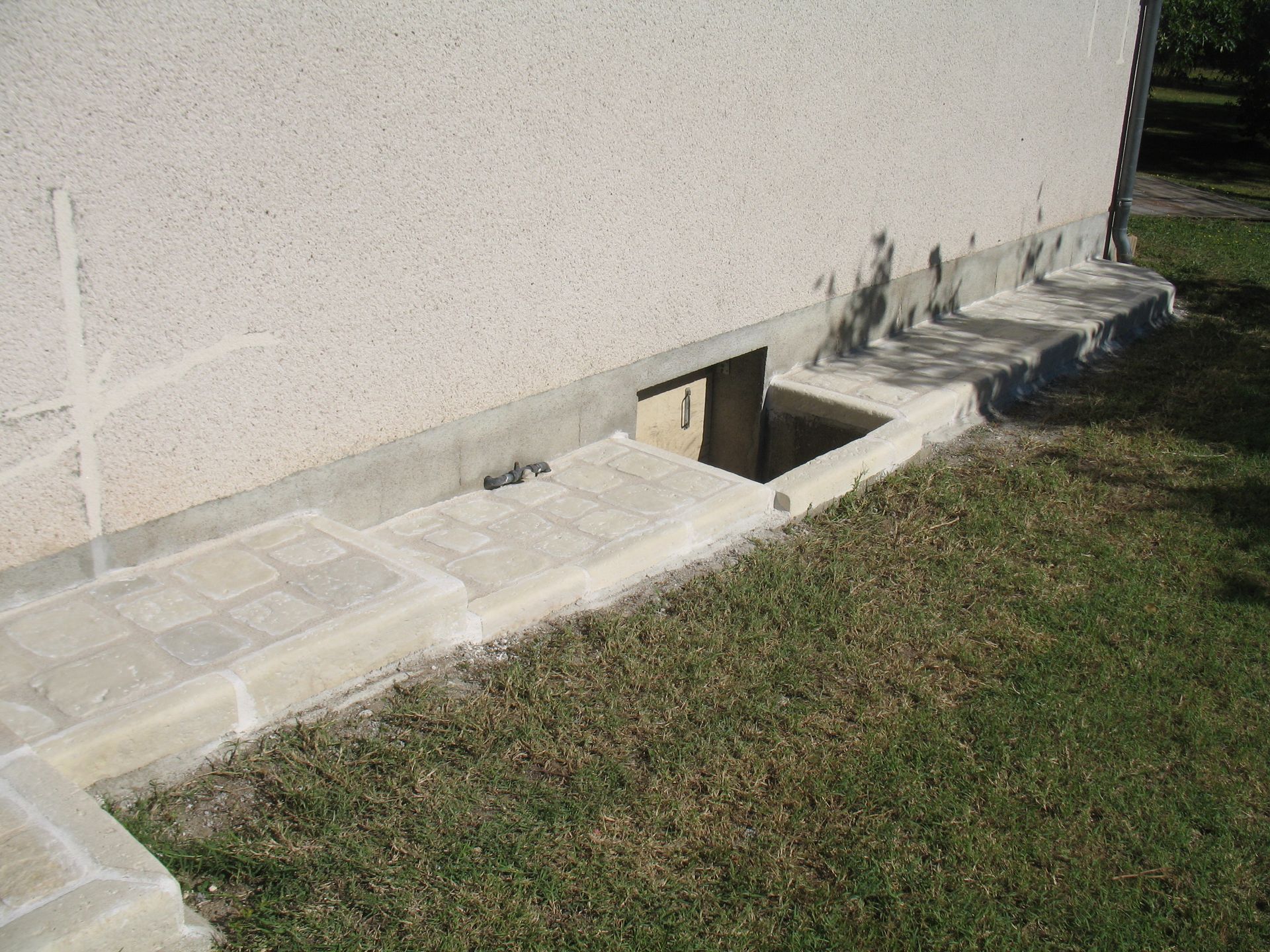 Vue extérieure d'un bâtiment avec une petite fenêtre au sous-sol et un escalier en béton menant à l'étage.