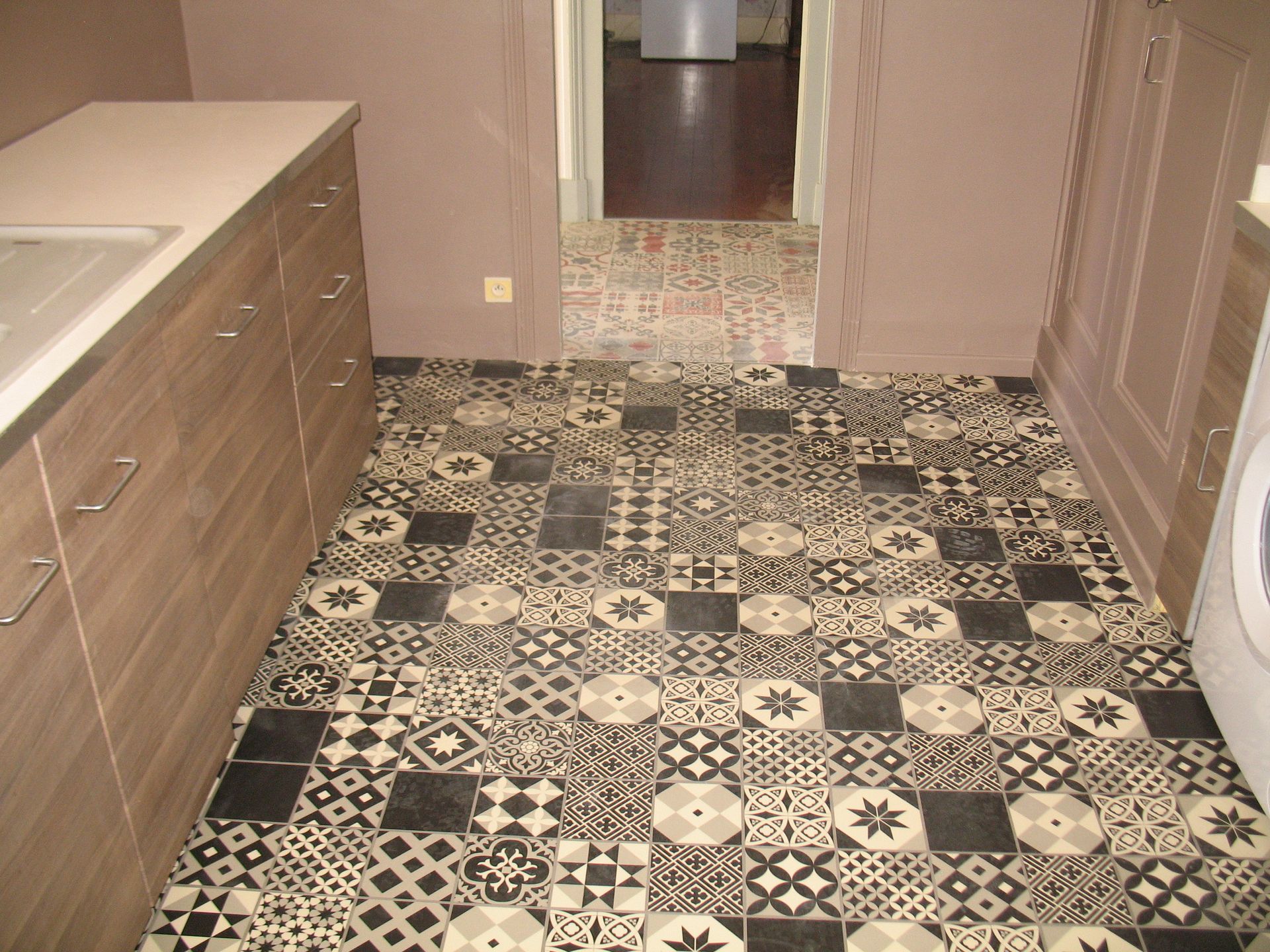Cuisine avec sol en carrelage à motifs, armoires et porte menant à une autre pièce.