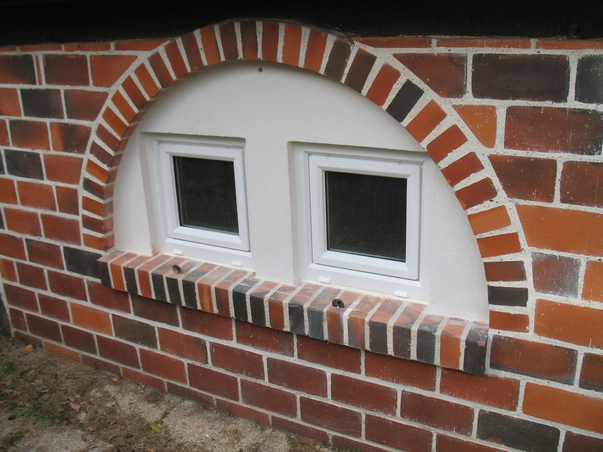 Mur de briques avec cadre de fenêtre en arc abritant deux fenêtres carrées.
