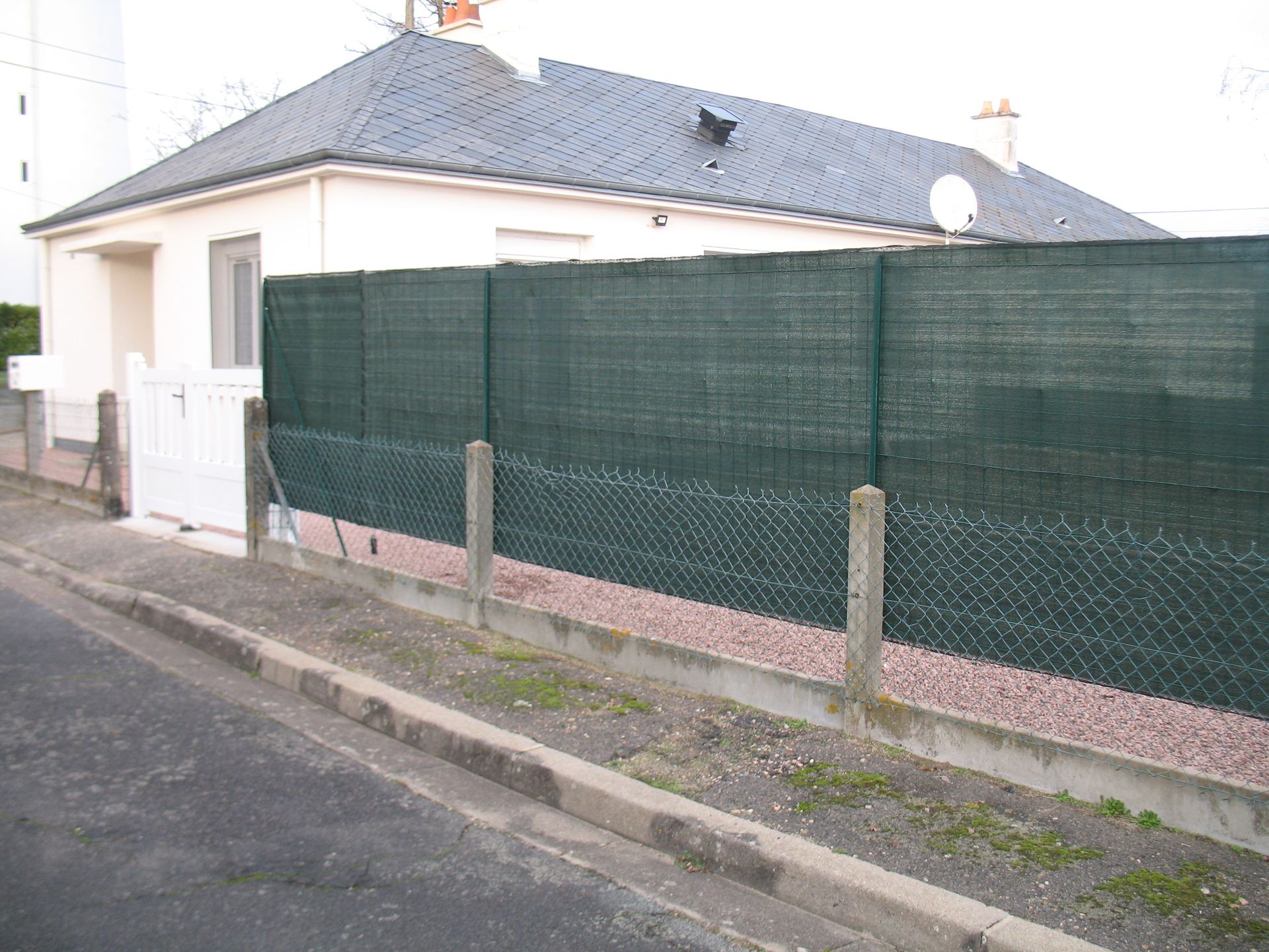 Une maison derrière une clôture en treillis vert le long d'un trottoir.
