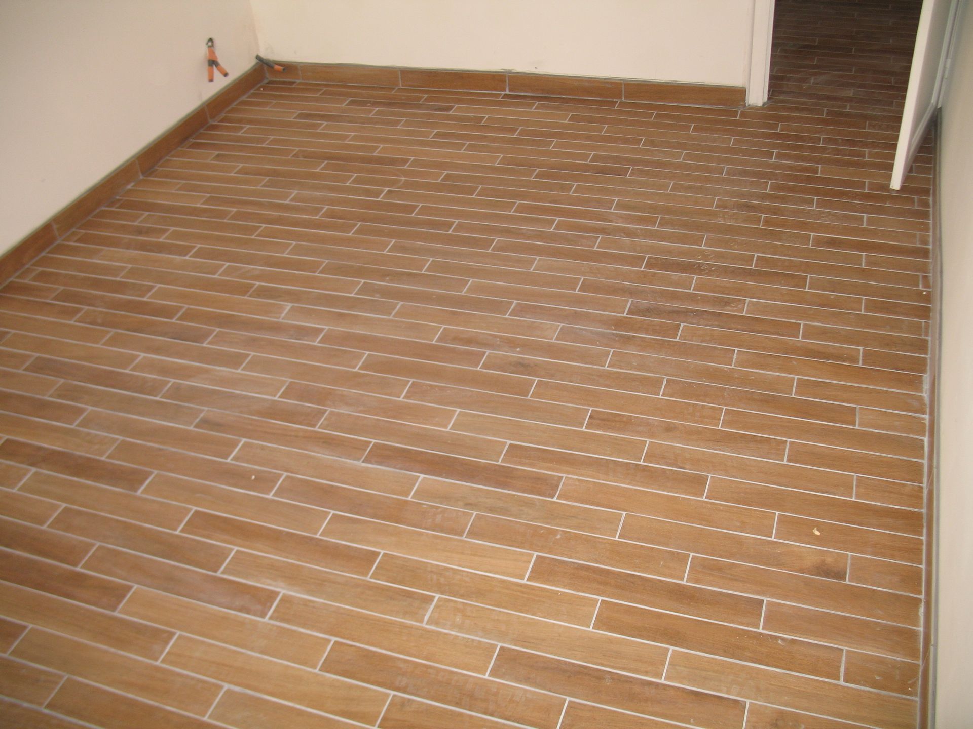 Des carreaux rectangulaires marron recouvrent le sol d'une pièce. Des joints blancs séparent les carreaux.