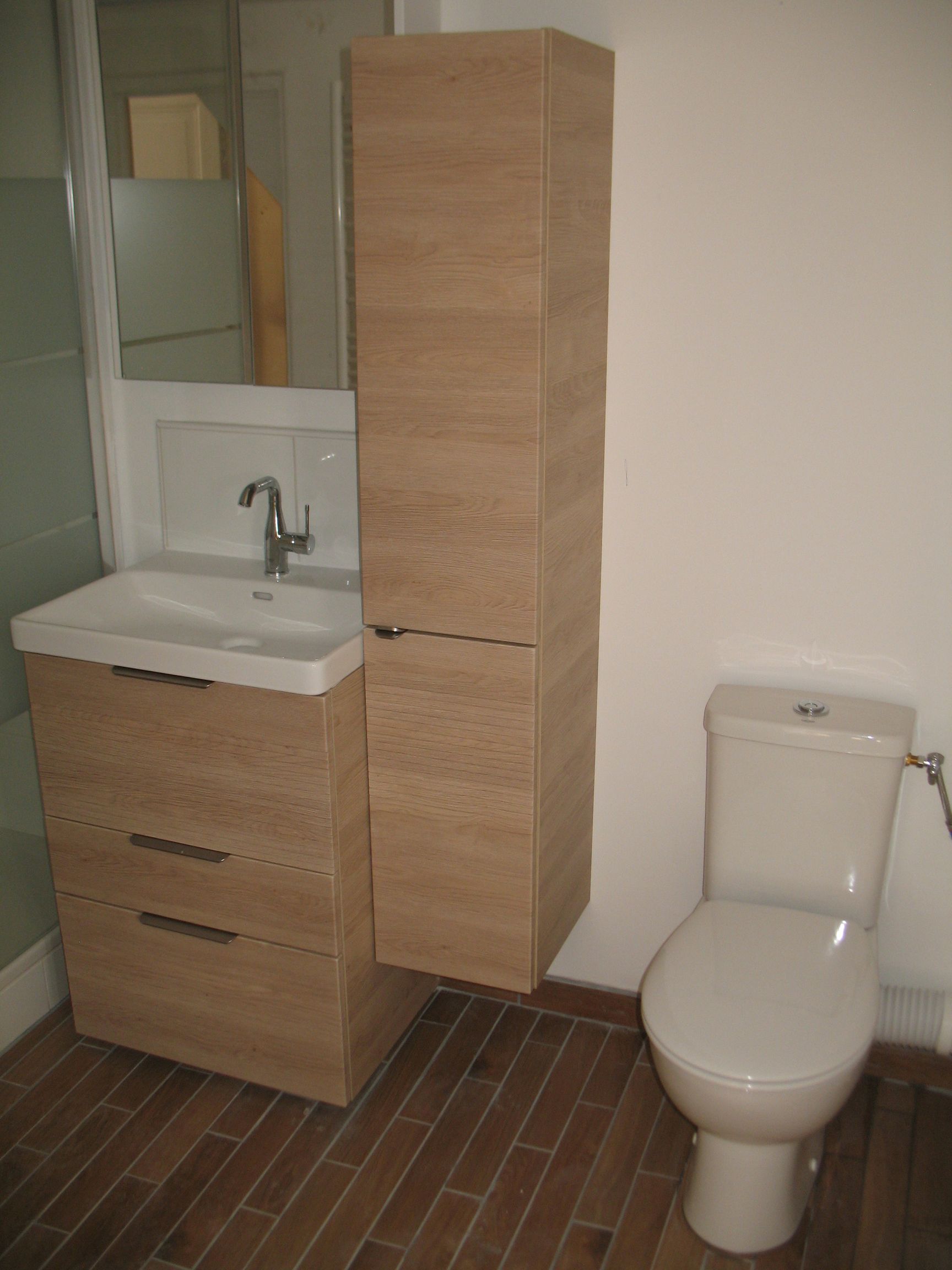 Salle de bain avec vanité en bois clair, grande armoire de rangement, toilettes et miroir.