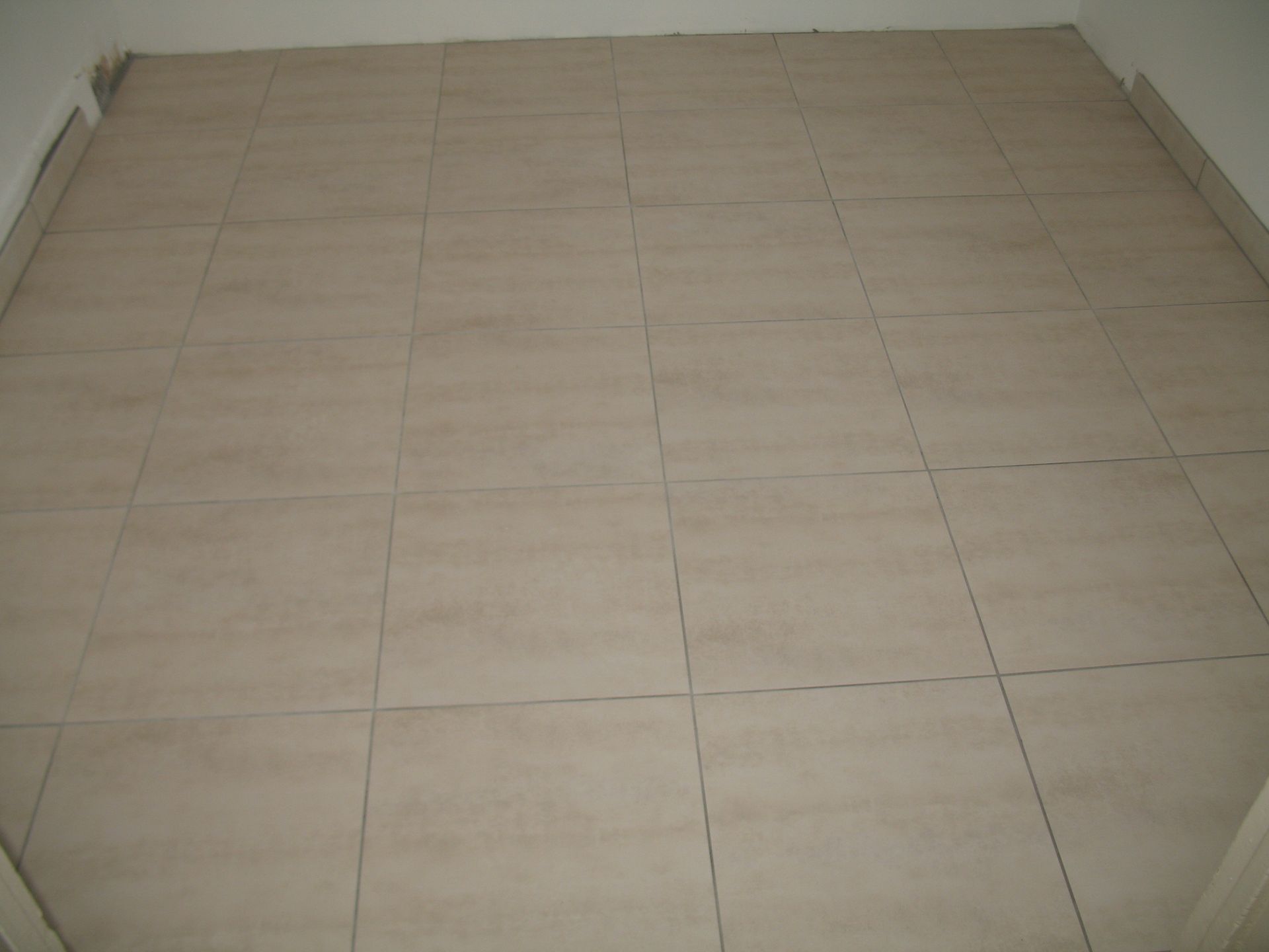 Carrelage beige dans une pièce, vu d'en haut. Des murs blancs bordent le sol.