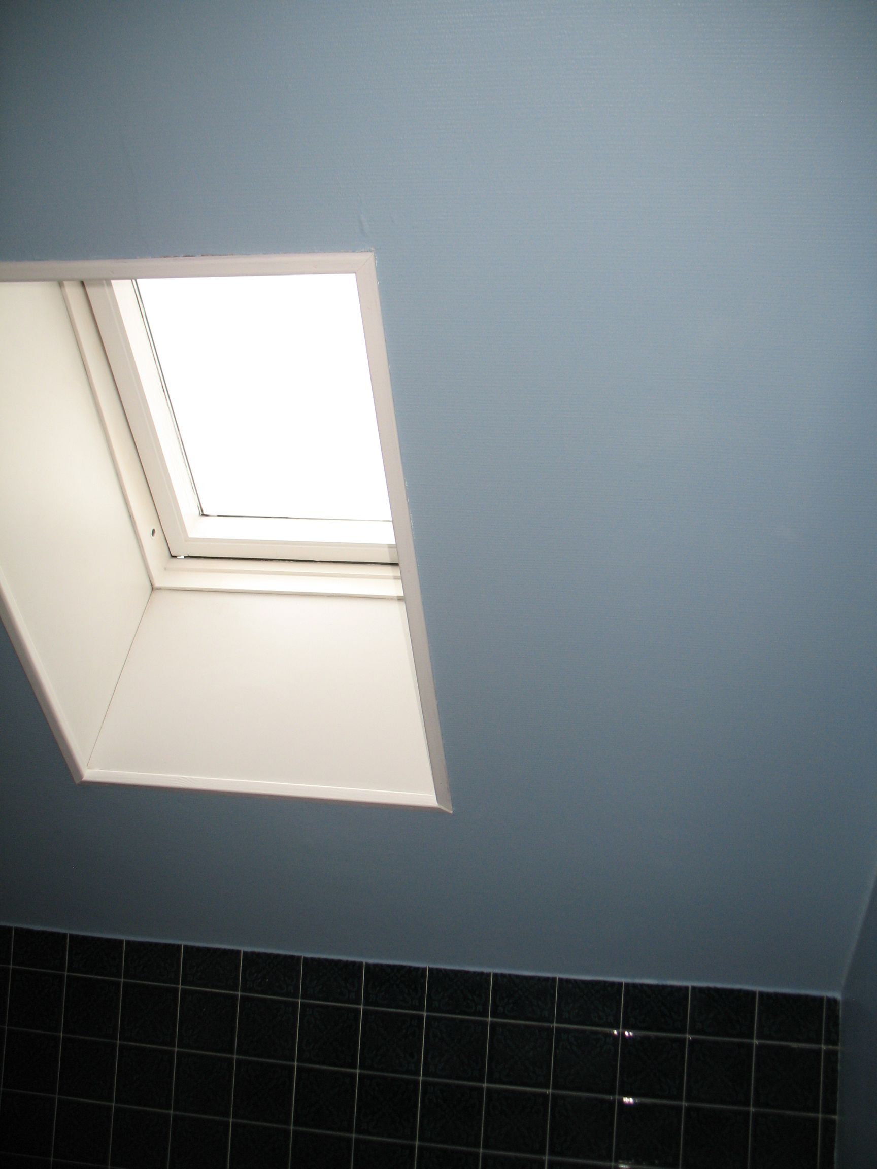 Puits de lumière dans une salle de bain aux murs bleus et carrelage noir.