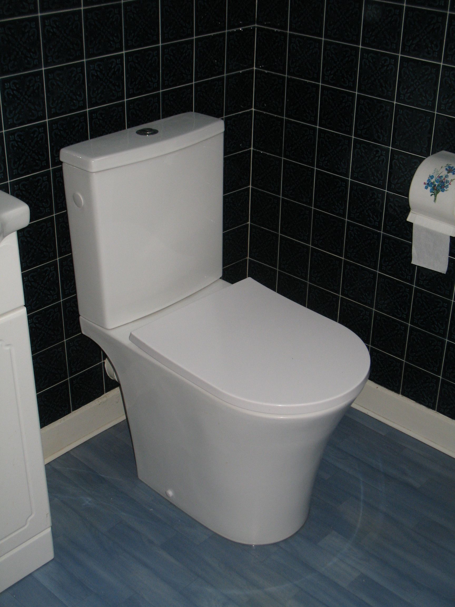 Toilettes blanches dans une salle de bain avec sol bleu et murs carrelés noirs.