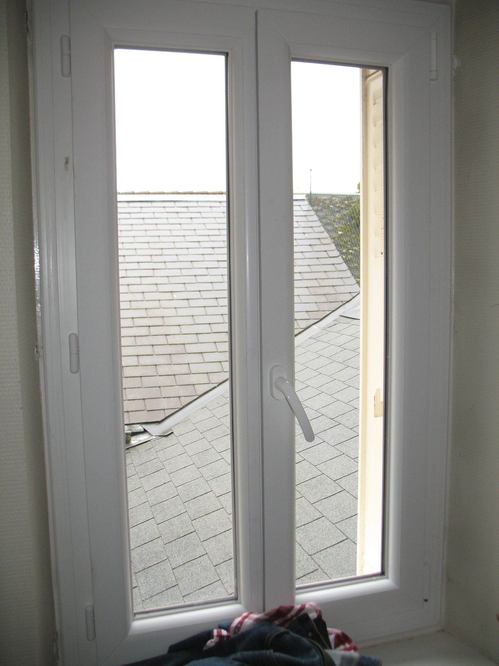 Fenêtre blanche, un seul panneau ouvert, donnant sur un toit gris.