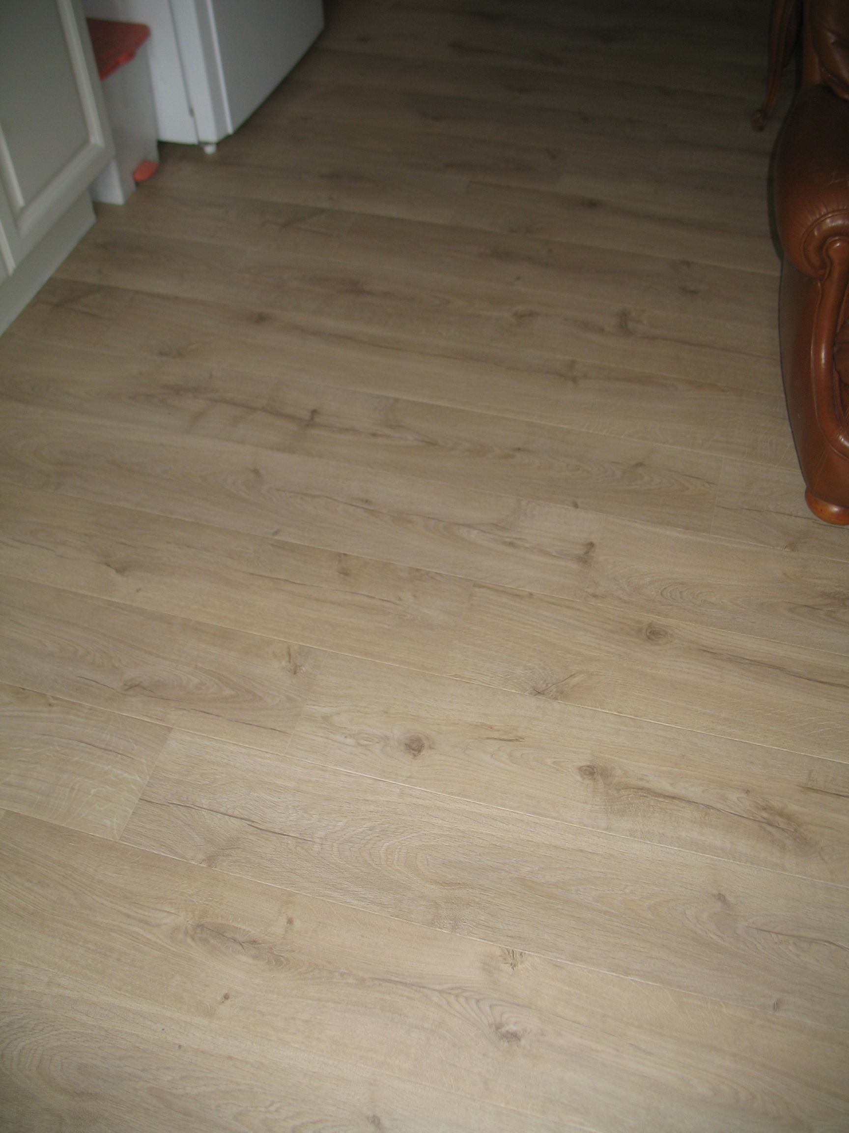 Plancher aspect bois marron clair avec quelques traces d'usure et petits nœuds, partiellement visibles.