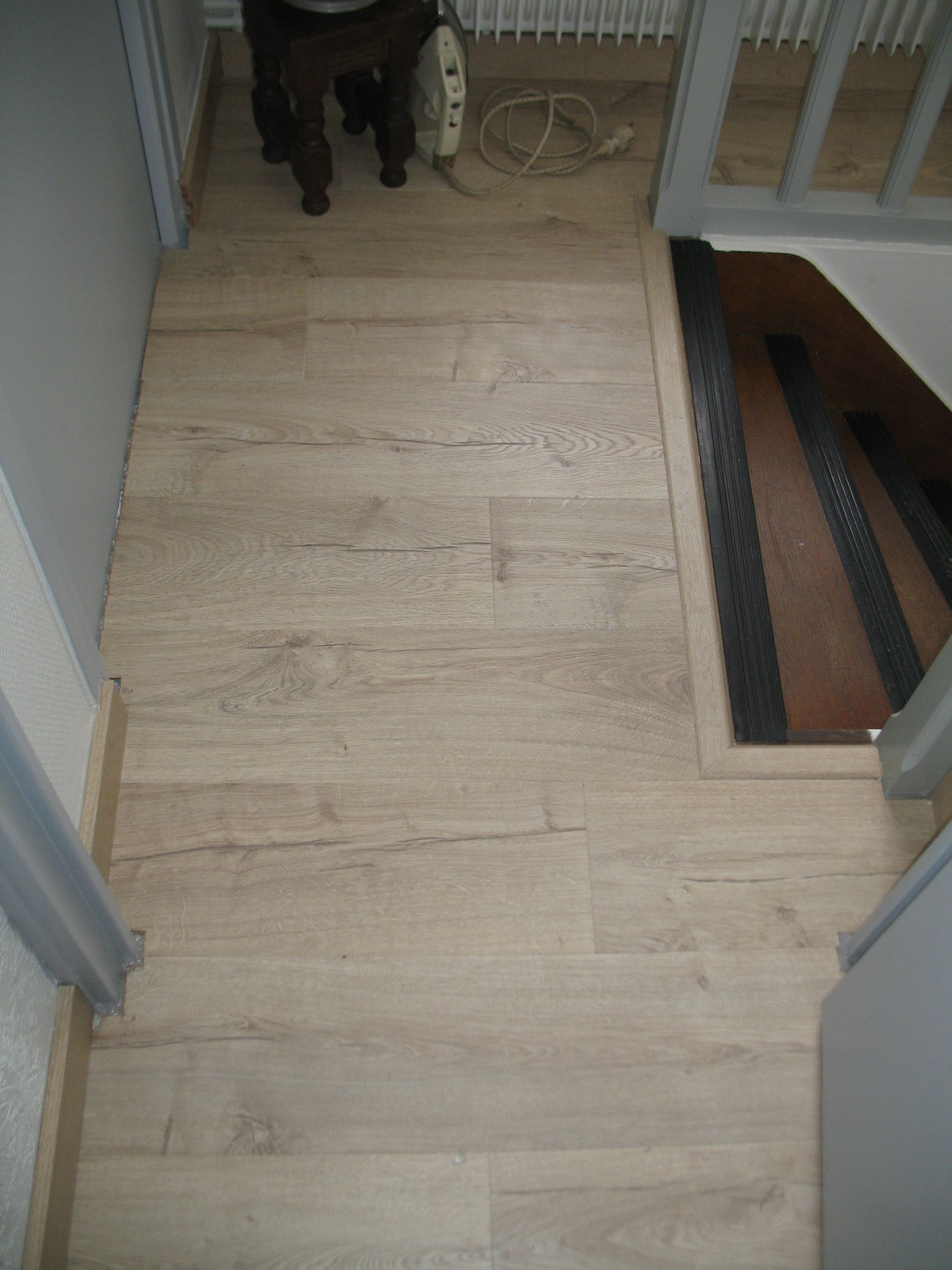 Parquet aspect bois clair dans un couloir avec cage d'escalier à droite.