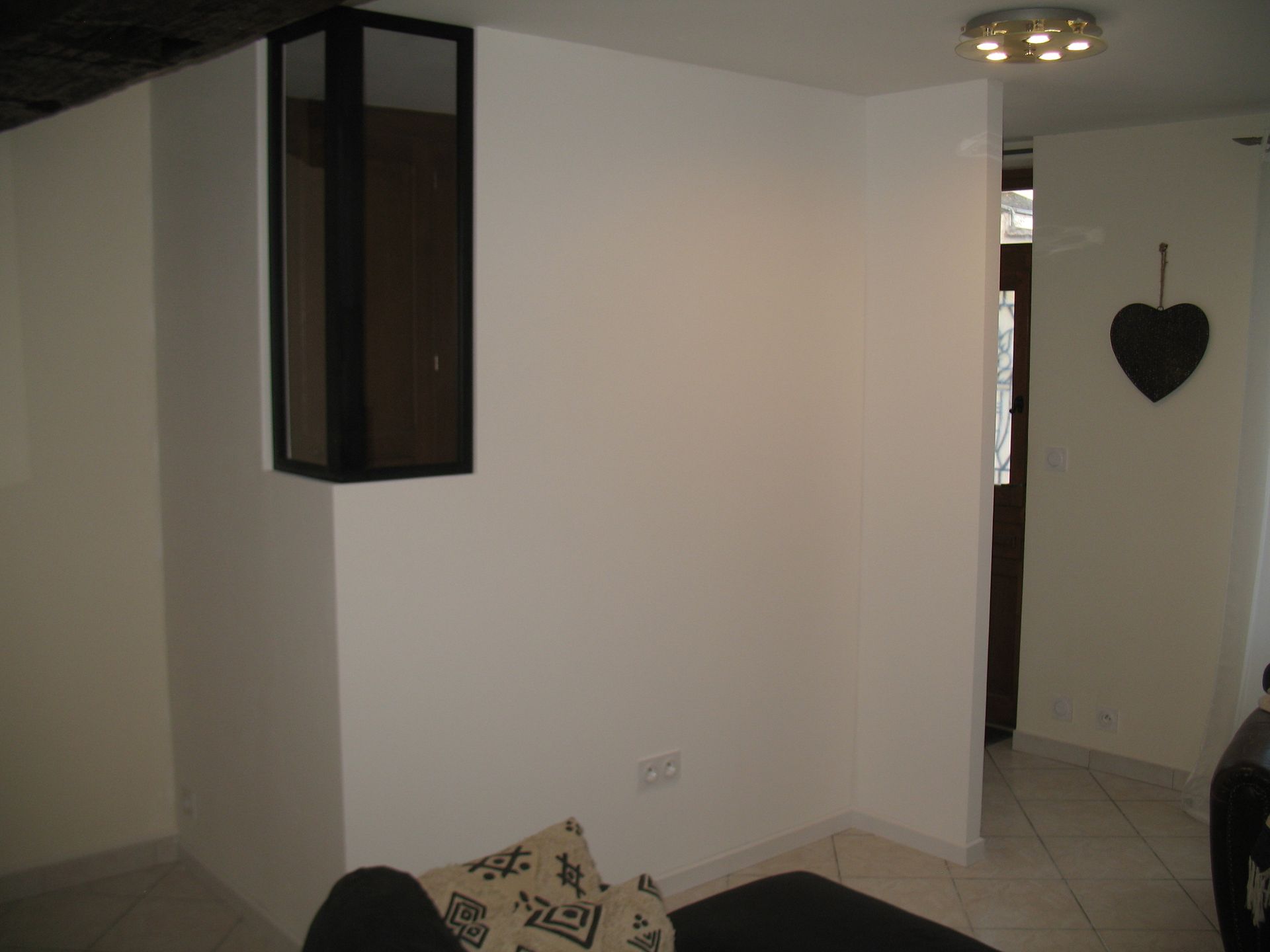 Murs blancs dans un coin avec une structure noire à gauche, une porte en arrière-plan et une décoration en forme de cœur.