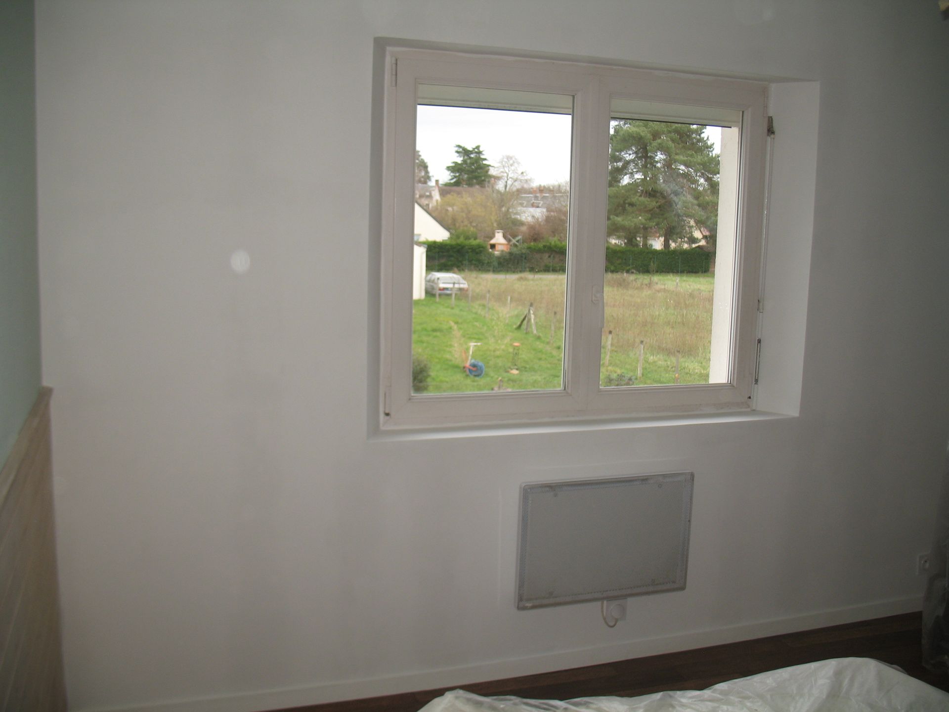 Fenêtre dans une pièce donnant sur une cour avec un radiateur en dessous.