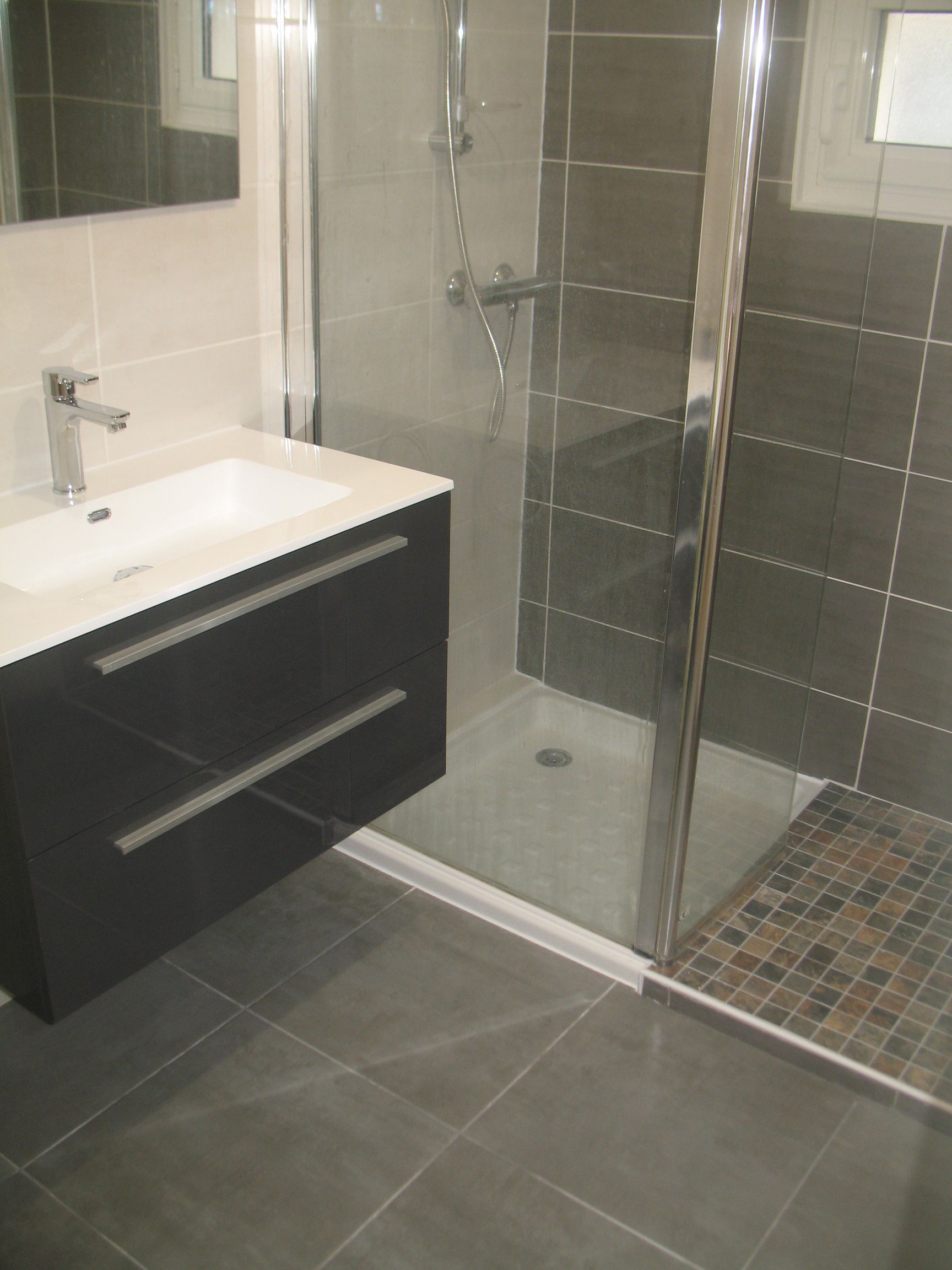 Salle de bain moderne avec vanité gris foncé, douche en verre et sol en carrelage gris.