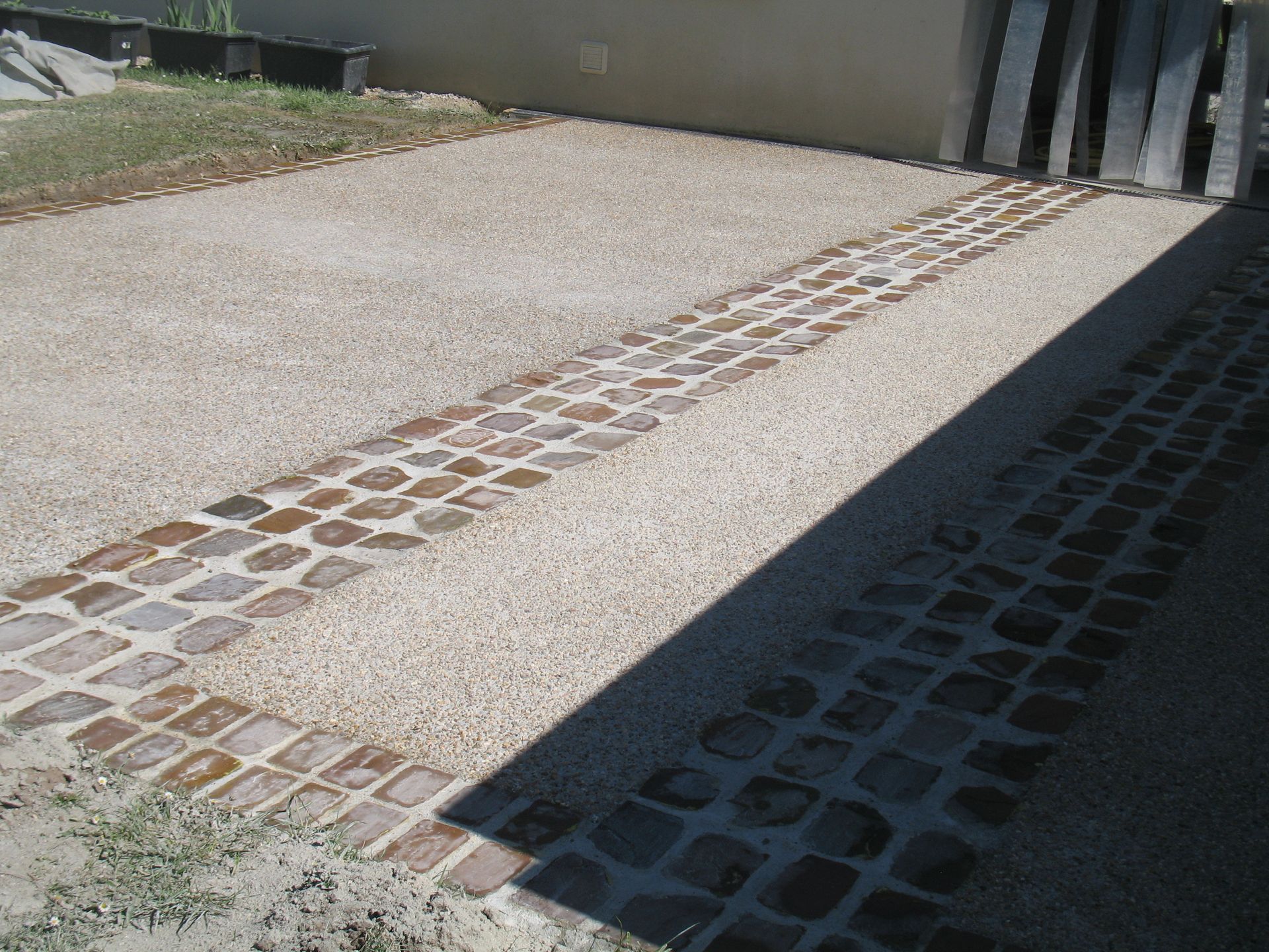 Allée en gravier avec bordure en briques et partiellement ombragée.