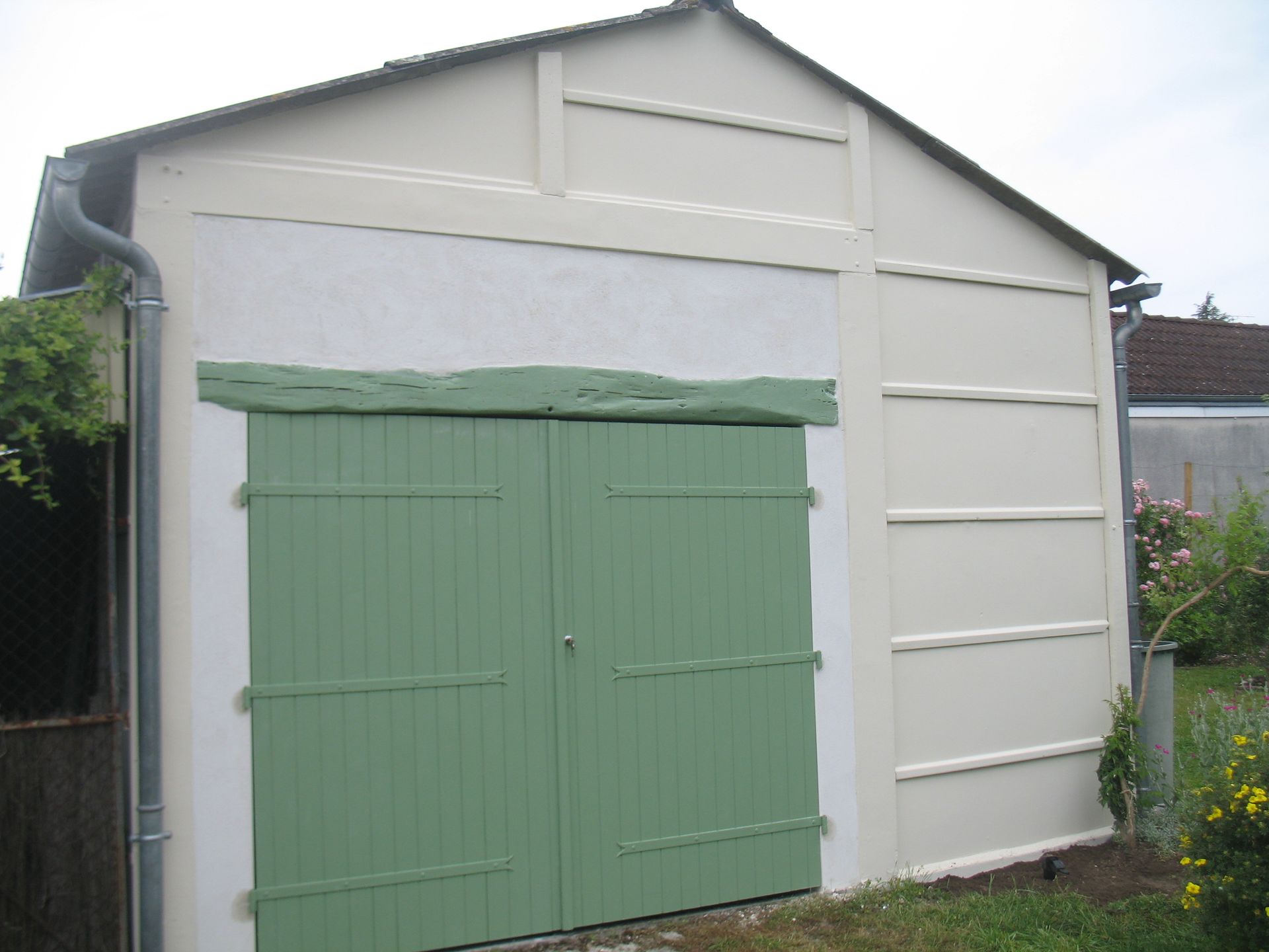 Portes de garage vertes sur un bâtiment de couleur claire, avec garniture beige et poutre d'accent verte.