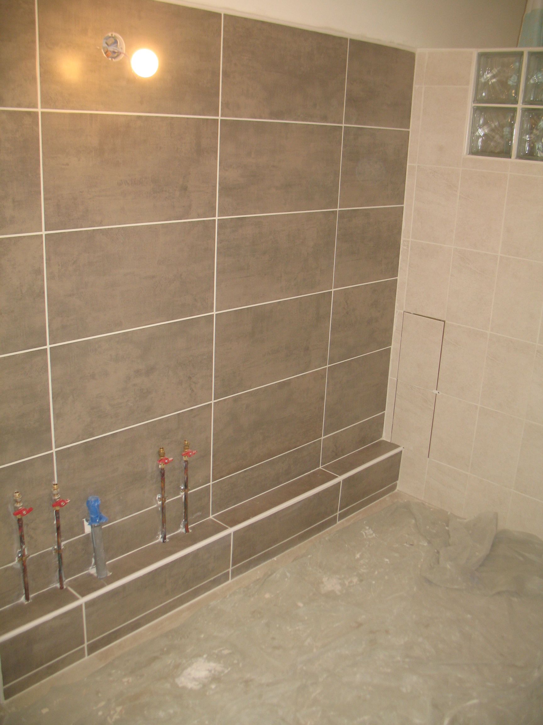Salle de bain avec carrelage marron sur les murs, la plomberie et le sol en béton.