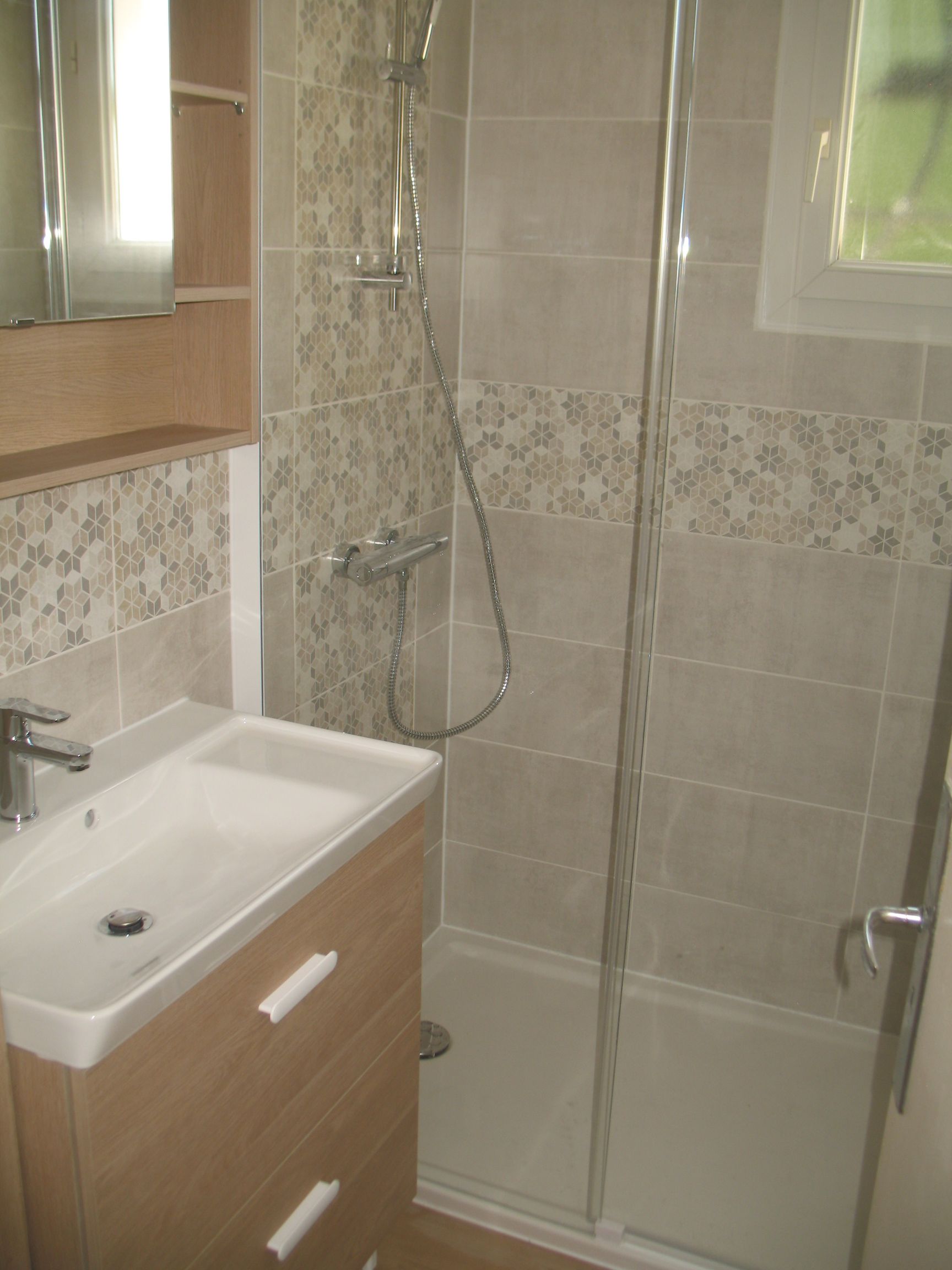 Salle de bain avec lavabo, douche et meuble en bois. Carrelage marron clair et gris.