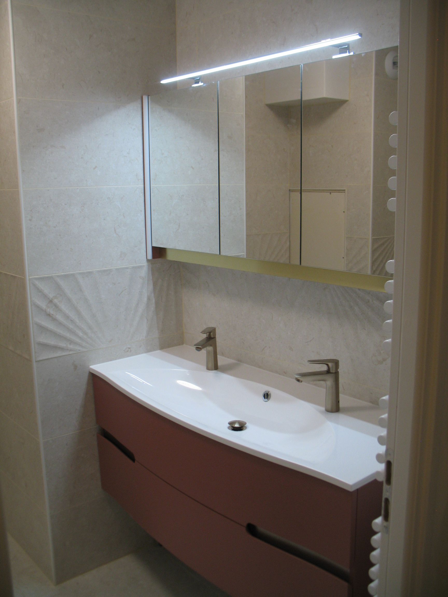 Salle de bain moderne avec vanité rose, deux lavabos, armoire à miroir et un accent mural décoratif.