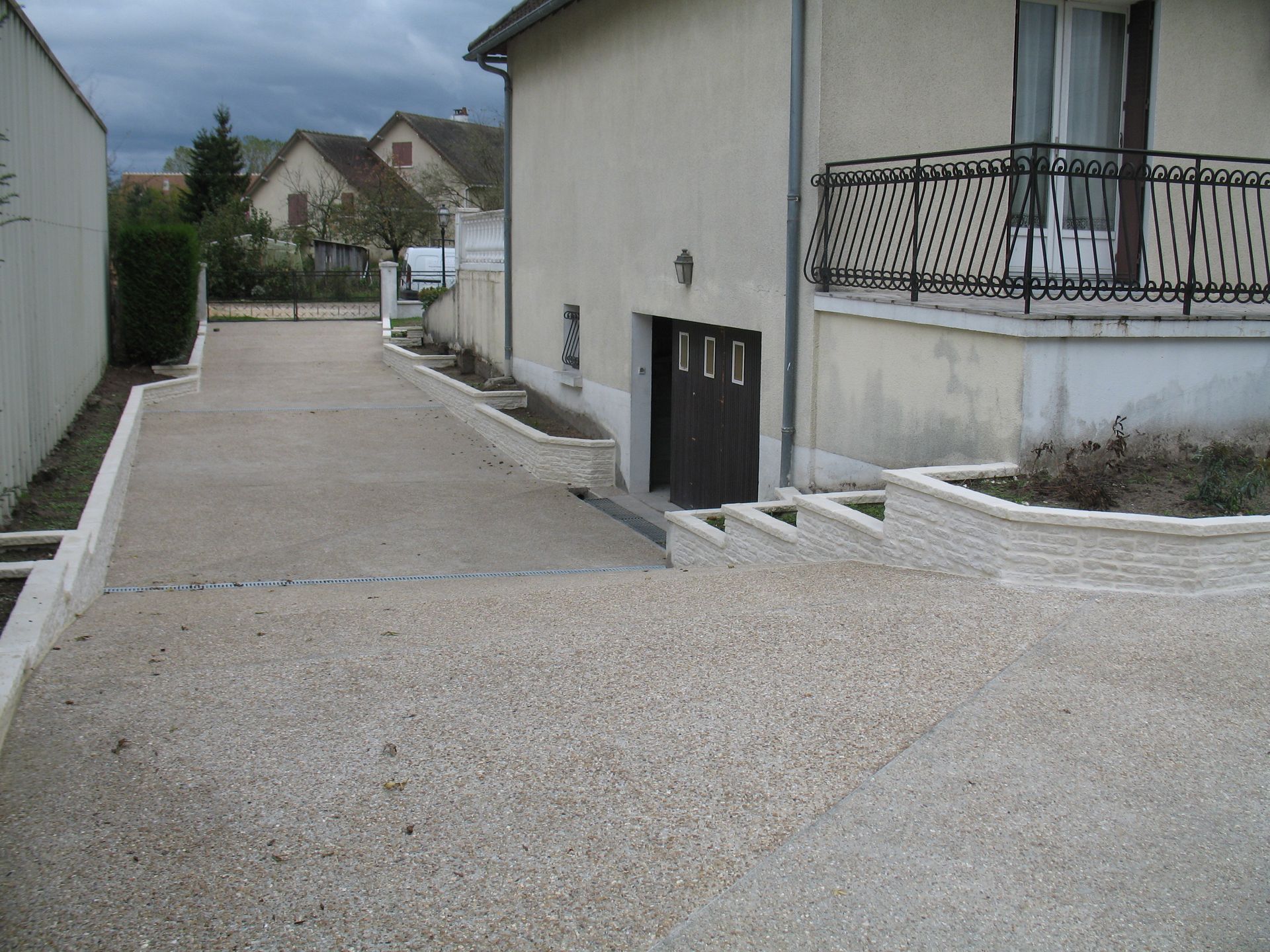 Allée menant à un bâtiment beige avec un balcon en fer forgé; ciel couvert.