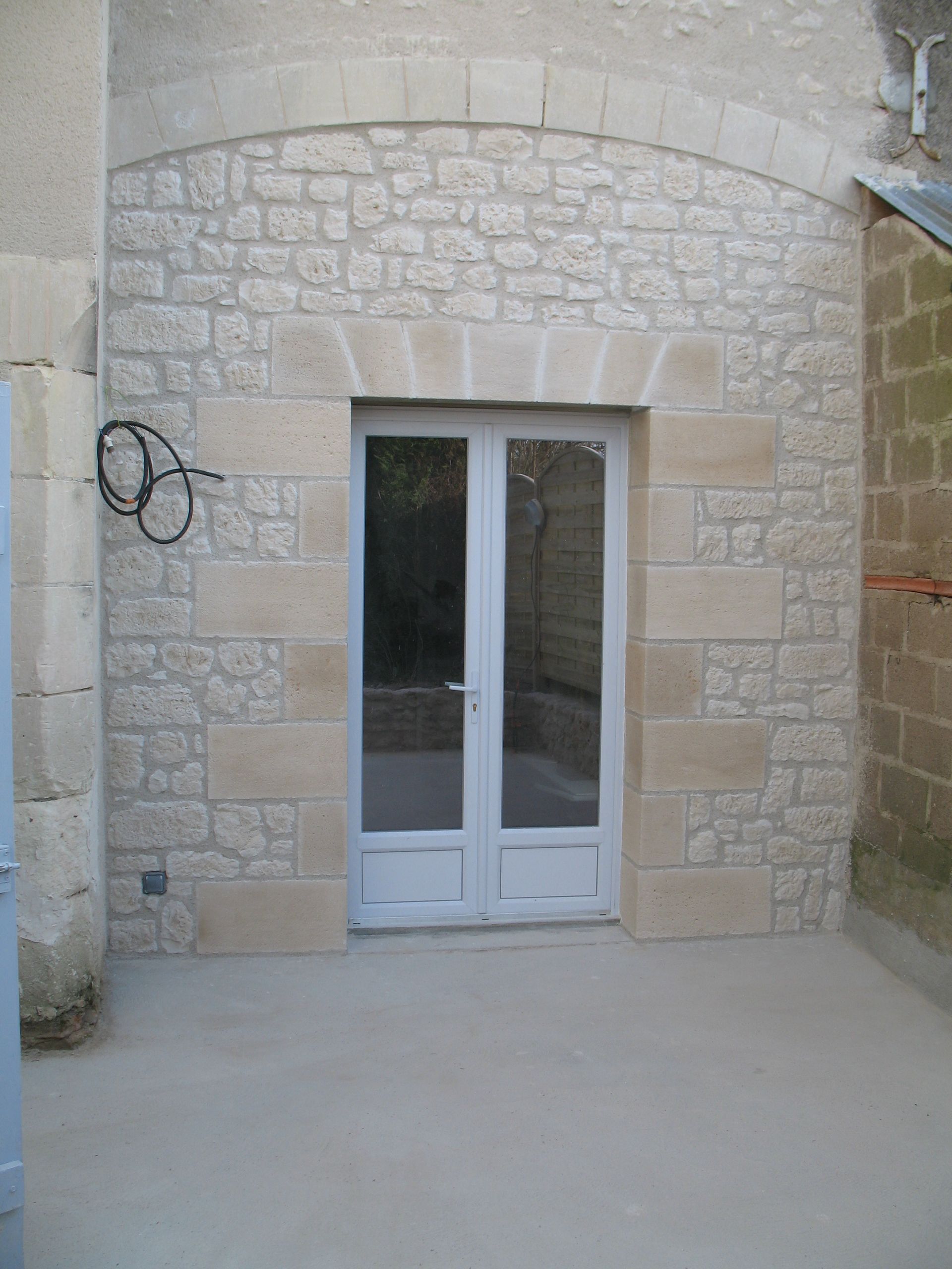 Une arche en pierre encadre une porte double. Mur extérieur en pierre brute.