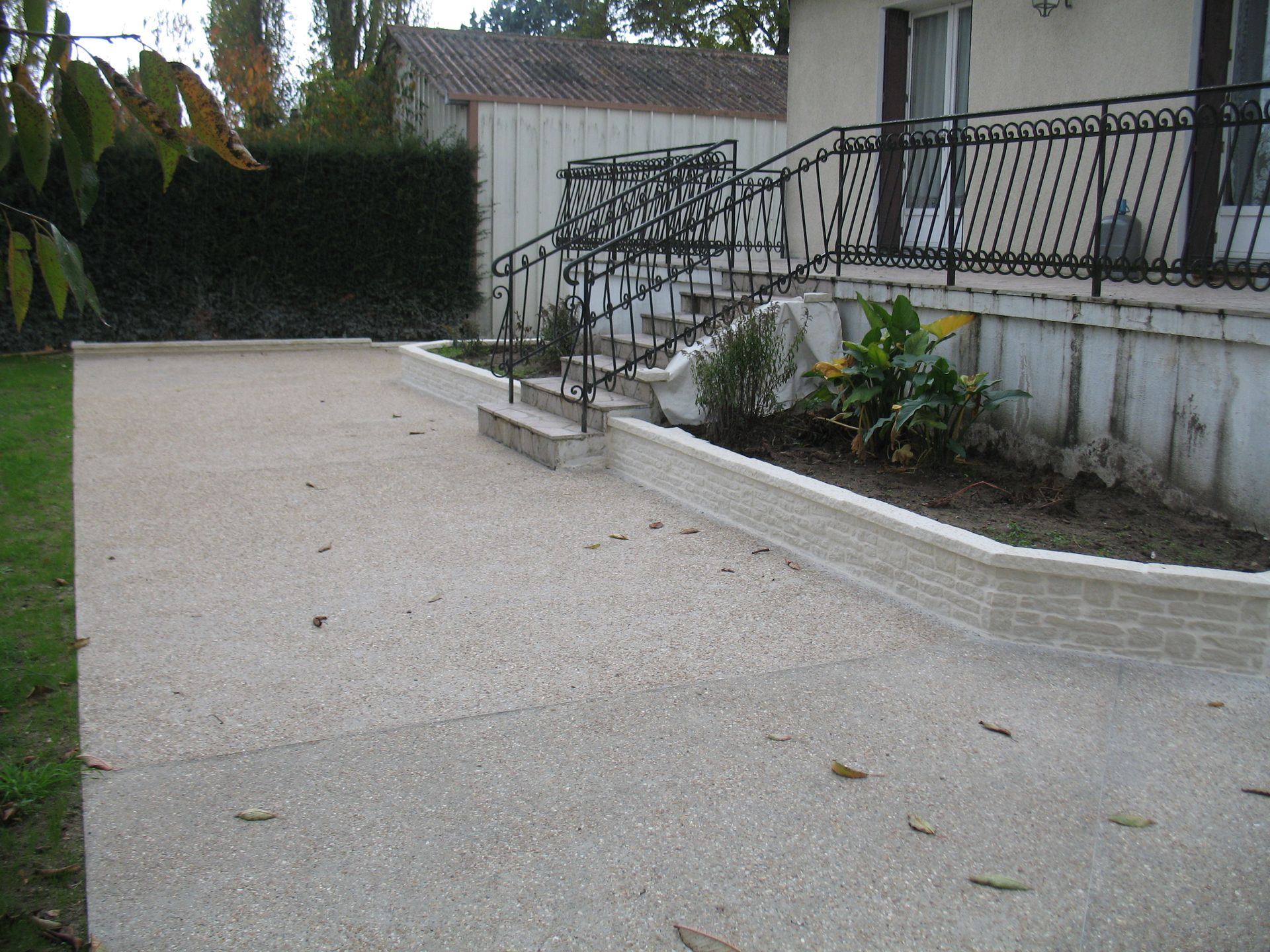 Une allée de gravier et un muret mènent à une maison avec des marches. Le ciel est couvert.