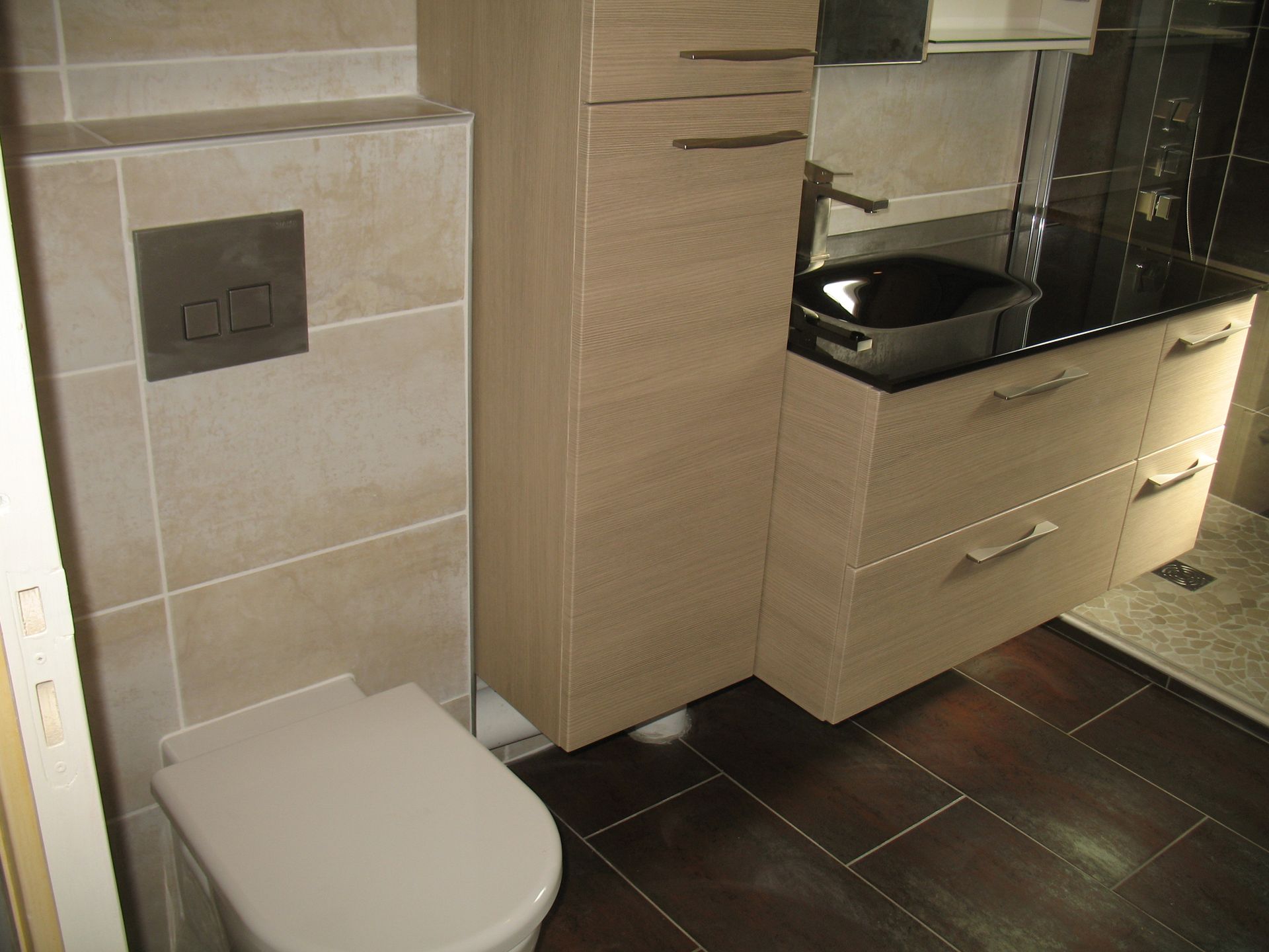 Salle de bains avec toilettes, lavabo et meubles en bois clair. Carrelage marron au sol et carrelage beige aux murs.