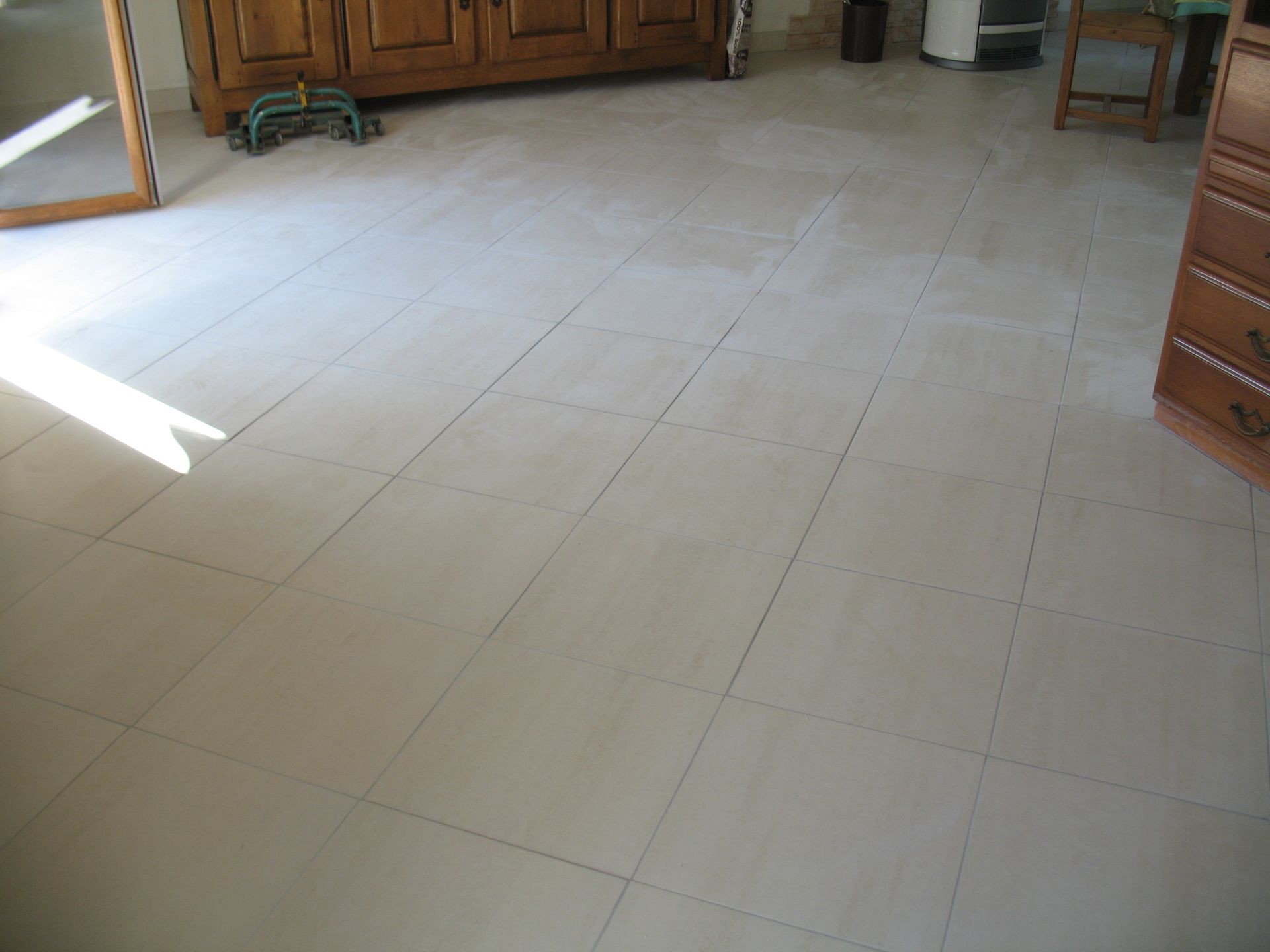 Carrelage clair avec joints foncés. Une commode et un placard en bois sont visibles dans une pièce.