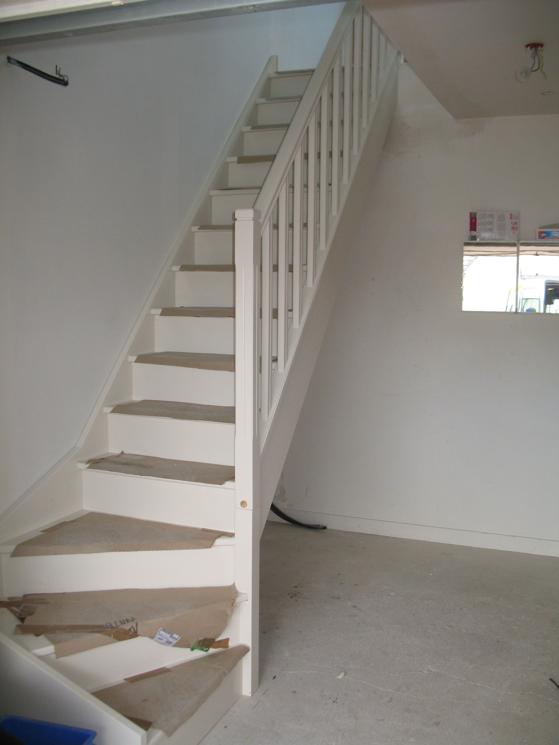 Escalier peint en blanc, menant à un deuxième niveau, dans une pièce aux murs blancs.