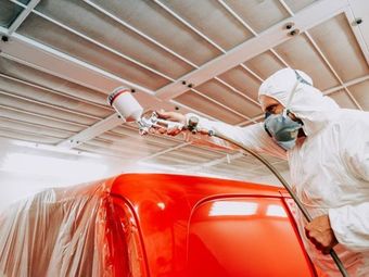 Un hombre está pintando con aerosol una camioneta roja en un garaje.
