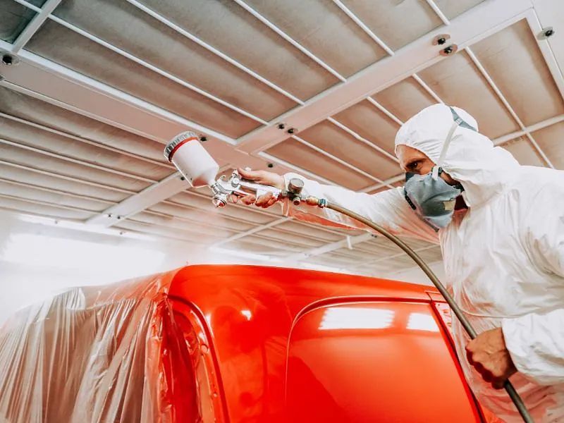 Un hombre está pintando con aerosol una camioneta roja en un garaje.