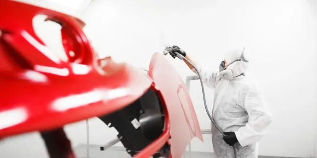 Un hombre está pintando un coche rojo en una cabina de pintura.