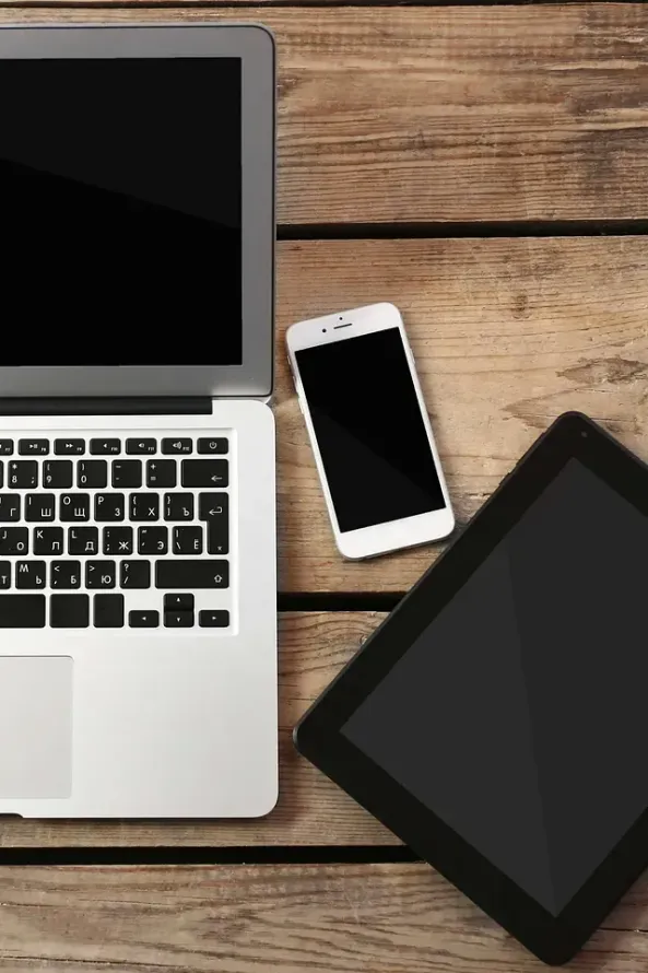 Una computadora portátil, un teléfono celular y una tableta están sobre una mesa de madera.