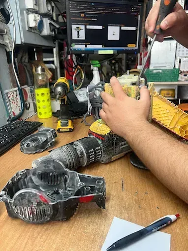 Un técnico utiliza un destornillador para reparar una herramienta eléctrica amarilla desmontada en un banco de trabajo 