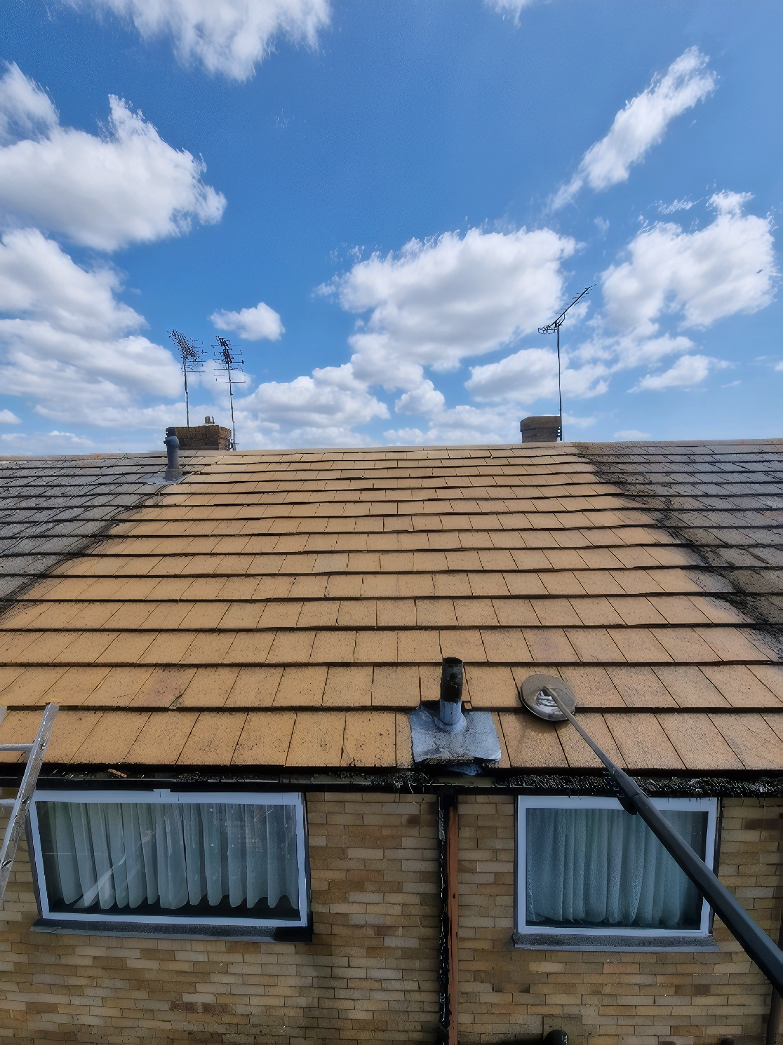 Brick house roof under repair with tan shingles against a blue sky with clouds