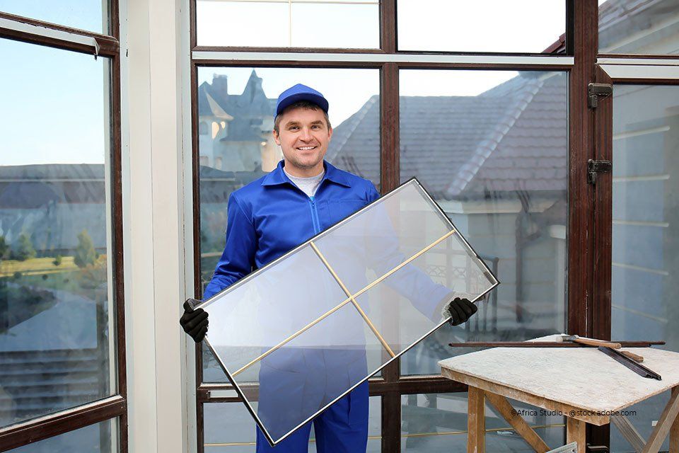 Mitarbeiter der Aacotec Glasereigesellschaft mbH lacht und hat Glasscheibe in der Hand