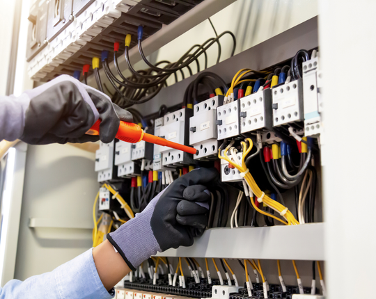 Un électricien travaille sur un boîtier électrique avec un tournevis.