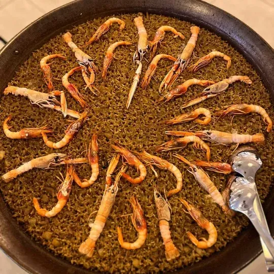 Una sartén llena de camarones y arroz con una cuchara dentro.