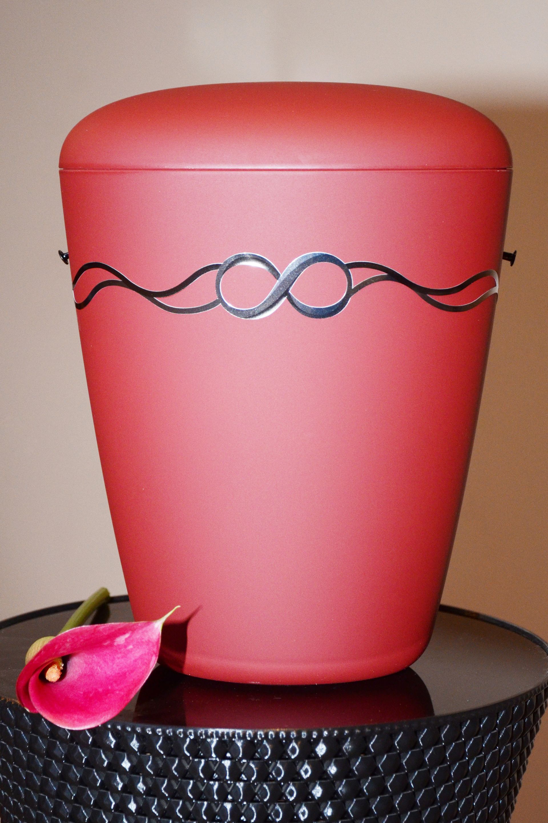 Rote Urne mit Unendlichkeitssymbol-Design, rosa Blume auf schwarzem Tisch
