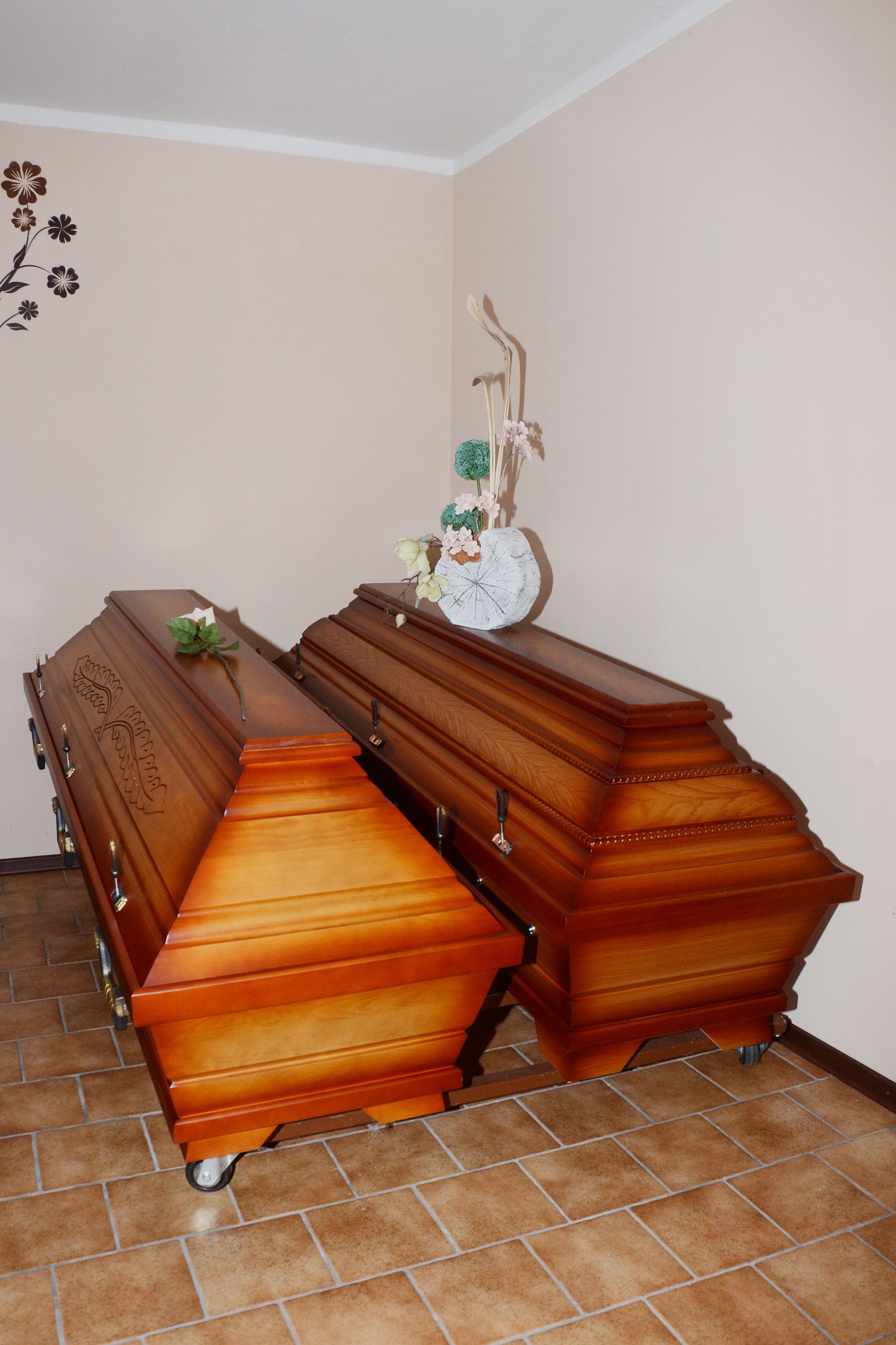 Zwei geschlossene Holzsärge mit Blumenarrangements in einem Raum