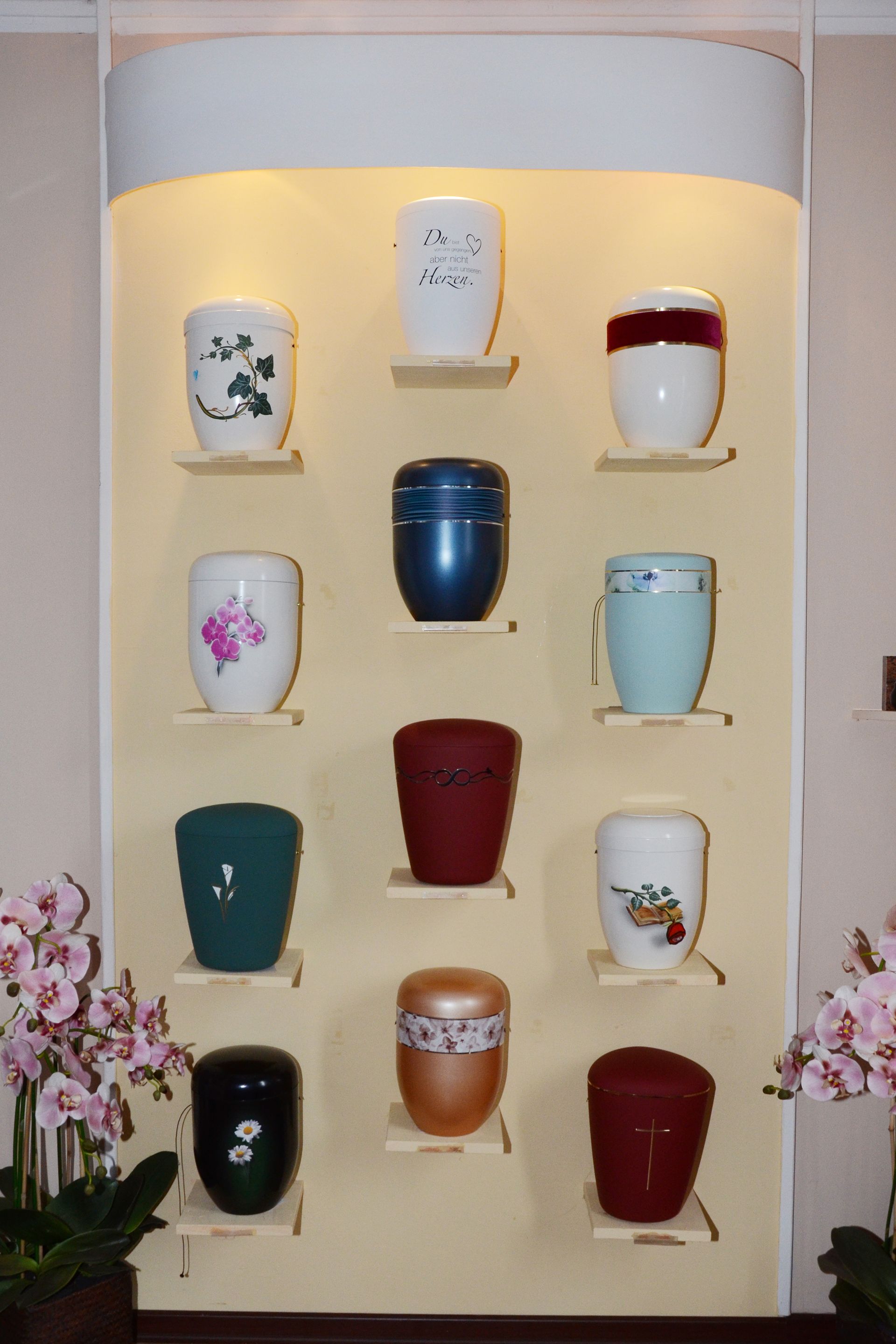Ausstellung von Keramikurnen in verschiedenen Farben und Designs auf Regalen in einem Ausstellungsraum