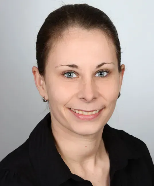 Eine Frau in schwarzem Hemd und Ohrringen lächelt in die Kamera