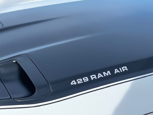 Gros plan sur le capot d'une voiture avec l'inscription « 429 RAM AIR » et une bande noire sur fond blanc.
