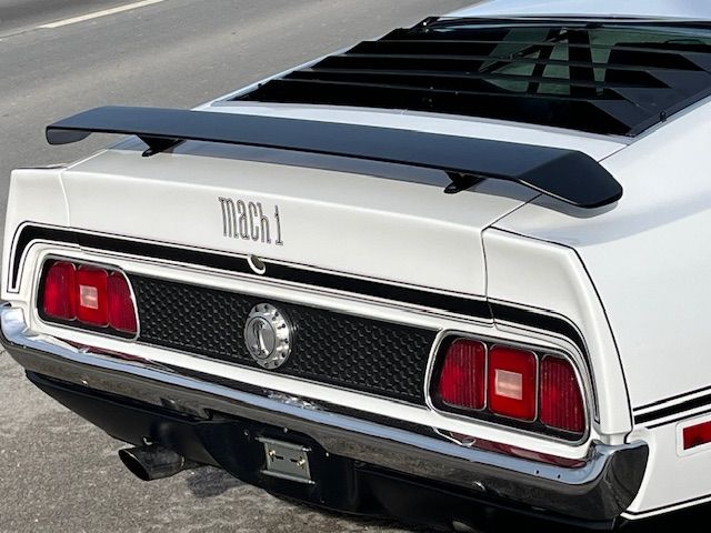 Arrière d'une Ford Mustang Mach 1 blanche de 1971 avec aileron et persiennes. Logo « Mach 1 » sur le coffre.
