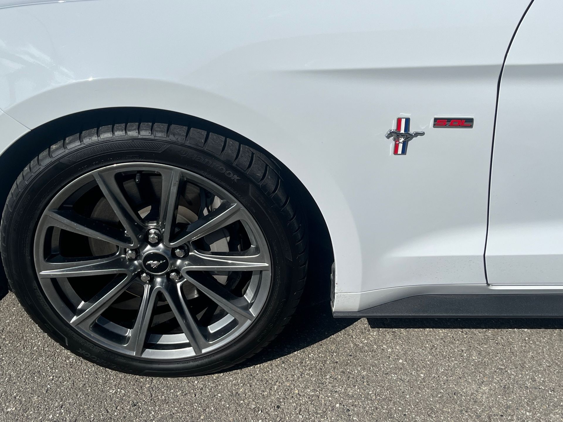 Gros plan sur la roue arrière et l'emblème latéral d'une Ford Mustang blanche.